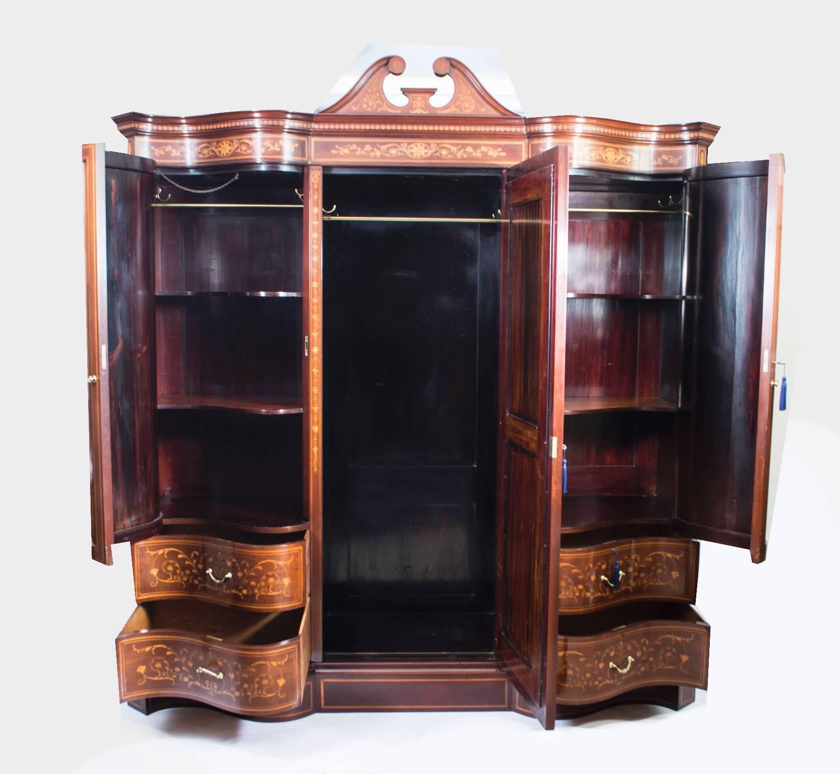 This is a spectacular antique late Victorian mahogany and floral marquetry serpentine shaped wardrobe bearing the engraved brass plaque of the renowned cabinet maker and retailer Edwards & Roberts, circa 1880 in date. It is inlaid with a