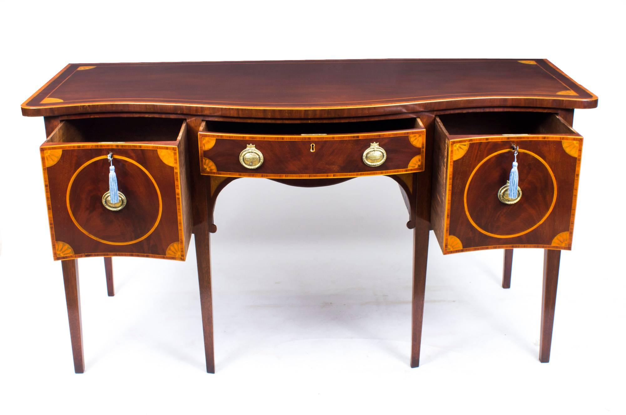 This is a superb Sheraton style flame mahogany serpentine sideboard with beautiful crossbanded and fan inlaid decoration, circa 1870 in date.

It has a central frieze drawer which is flanked by deep drawers, all with their original brass handles.