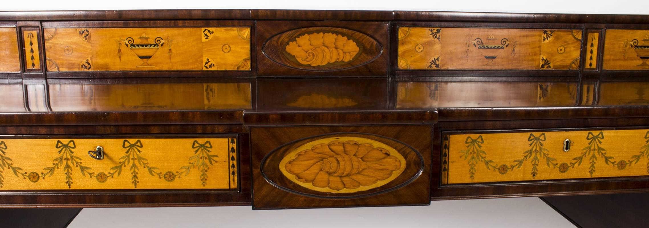 This is a superb antique Regency flame mahogany and satinwood Sheraton style inlaid sideboard, circa 1820 in date.

The shaped rectangular body features inlaid marquetry shells, classical urns and bellflower on geometric decoration. The stageback