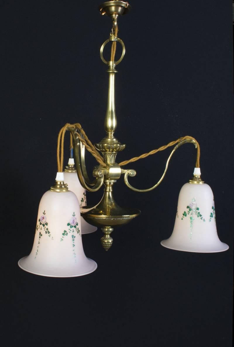 This is a beautiful antique cast brass three-light chandelier with glass shades that have been hand enamelled with garlands of flowers, in Art Nouveau design, dating from circa 1920.

These came from the hallway of a large 1920s house set behind a