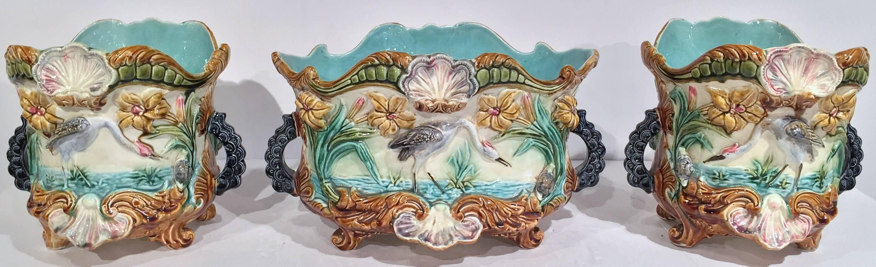 Beautiful set of three hand-painted and colorful Majolica cachepots with handles, circa 1870, featuring herons and flowers in relief. Excellent condition with vivid colors.