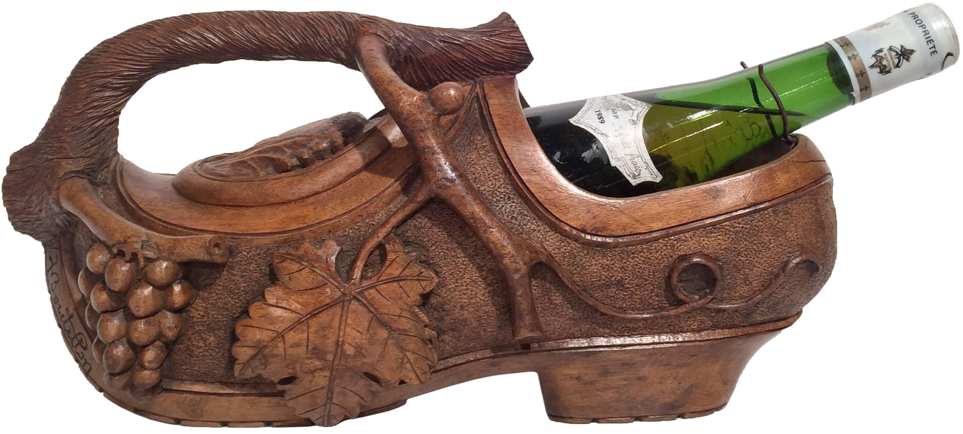 Impress your guests with this interesting antique wine bottle holder shaped as a clog shoe; crafted in France, circa 1920, the unique, hand carved bottle holder with handle shaped as vine, features high relief foliage decor throughout. The pouring