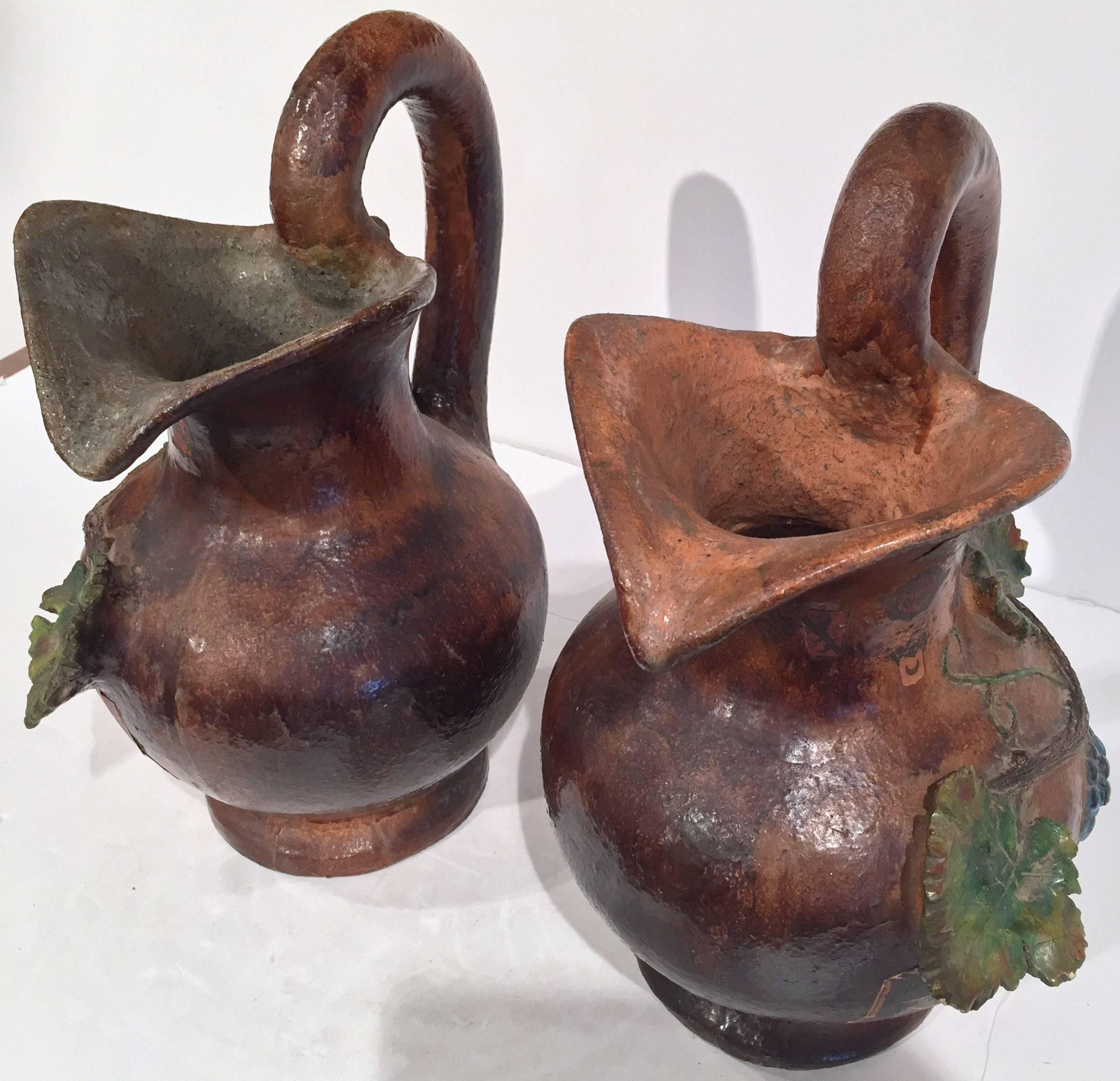 Enhance your wine cellar with this interesting pair of antique medieval terracotta wine pitchers from Bordeaux, France, circa 1860; the jugs made in clay, feature a large handle with a curved beak, and colorful relief grapes and vine leaves. Each