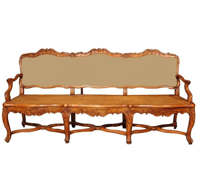 This elegant, antique, fruitwood bench was carved in Lyon, France circa 1890. The settee features eight cabriole legs with a triple X-bottom stretcher, a carved, serpentine apron and a triple arched back with hand-carved shell motifs. The bench has