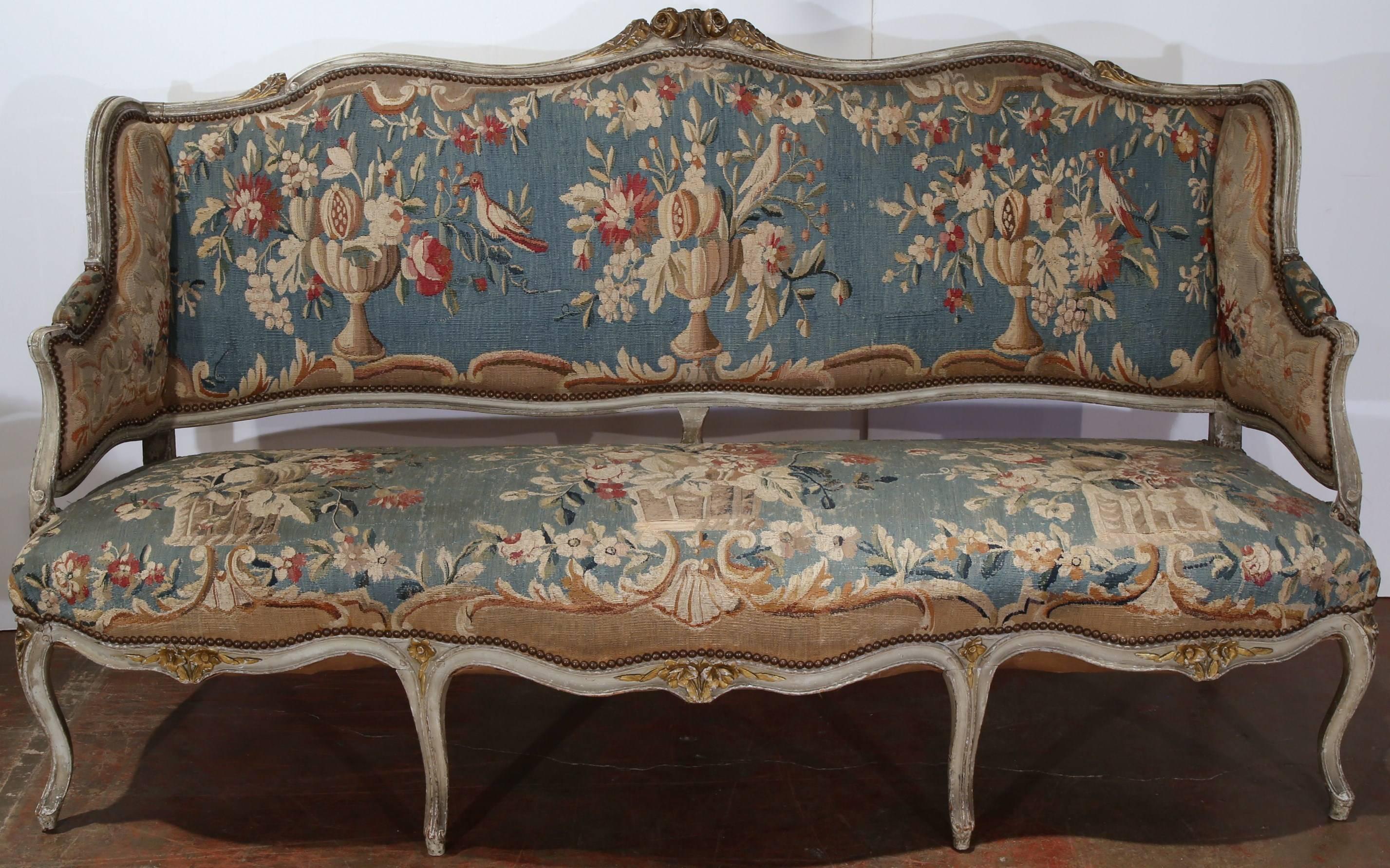 This elegant, antique painted settee was crafted in France, circa 1760. The classic French, Louis XV sofa features a shaped back with ear sides and sits on seven cabriole legs. The canapé is upholstered with its original Aubusson tapestry, which is