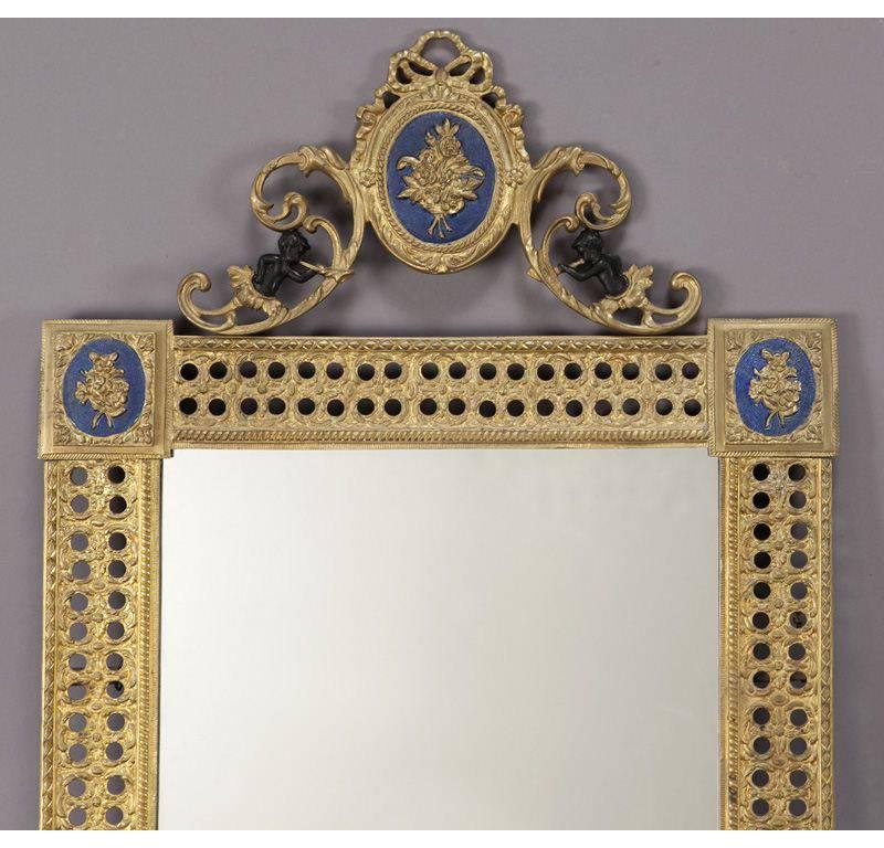 Place this elegant pair of Louis XVI bronze doré mirrors over a pair of consoles. Crafted in France, circa 1920, each pierced frame features an oval plate with blue enamel surmounted by scrolling crest and the traditional Louis XVI ribbon bow, and a