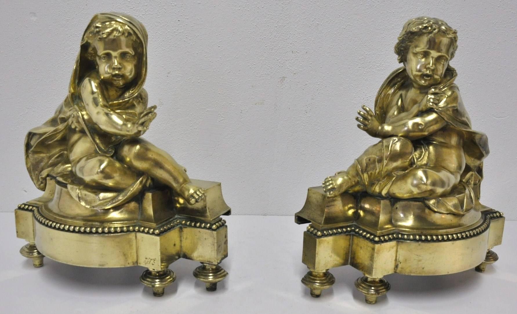 Pair of period antique bronze andirons with gilt finish from Paris, France.
Made during the reign of King Louis XVI, these chenets feature two small cupids wearing capes in a sitting position. With very fine details and angel faces, these pieces