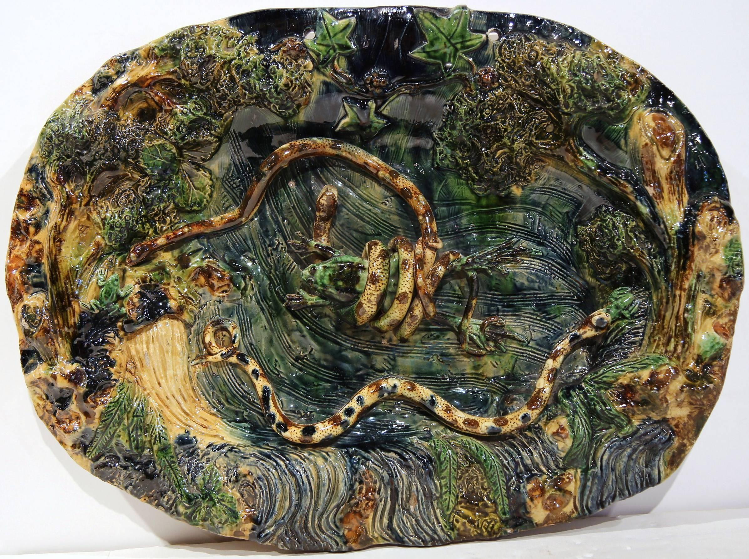 This colorful pair of antique hand-painted Majolica Palissy wall chargers were sculpted in Southern France, circa 1880. Each handcrafted ceramic plate is embellished with relief carvings of frogs, snakes and leaves. The rich green, blue and beige