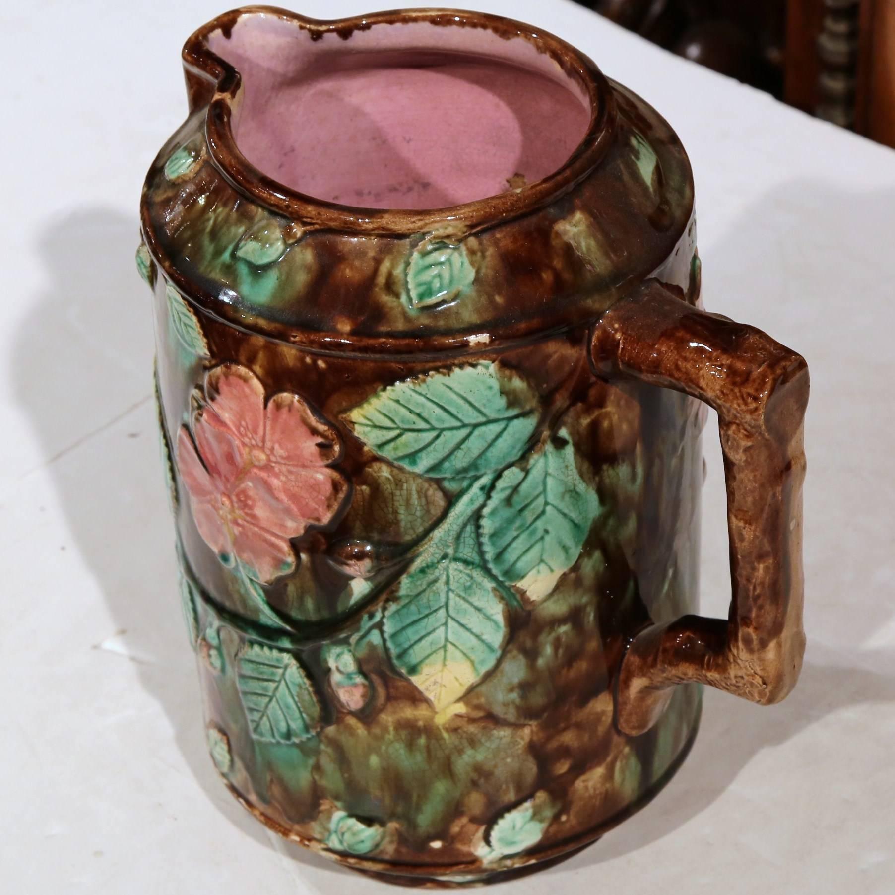 This colorful antique hand painted Majolica pitcher was crafted in France, circa 1870. The large ceramic water pitcher features a side handle, a pouring beek on the opposite side, and is embellished with green leaves, pink flowers and nuts. The