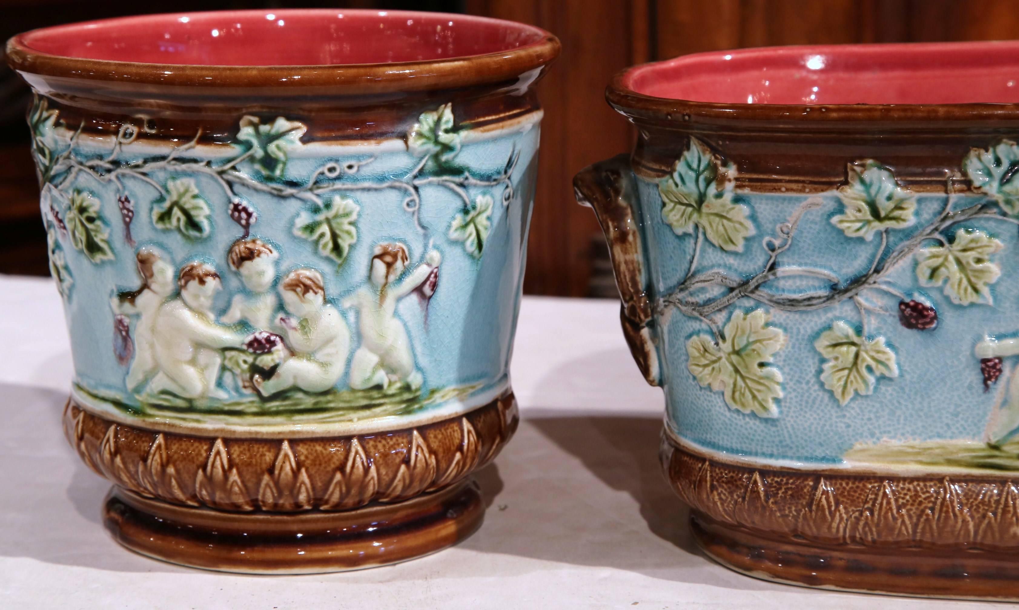 This fine antique set of majolica planters was crafted in France, circa 1880. Each ceramic cache pot depicts the reign of Bacchus thru scenes of young cherubs with vines and grapes. These colorful planters are in excellent condition with rich hand