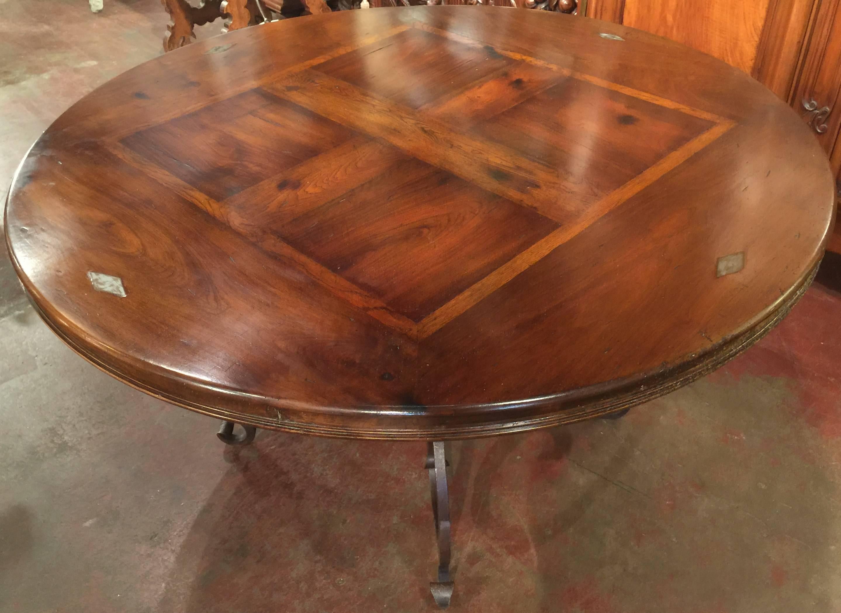 Elegant iron and wood round table from France. The thick walnut top made with antique wood, has a center parquet top and four large diamond shape decorative nails. Thick scrolled hand-forged iron base with a rust finish and some gilt. Excellent