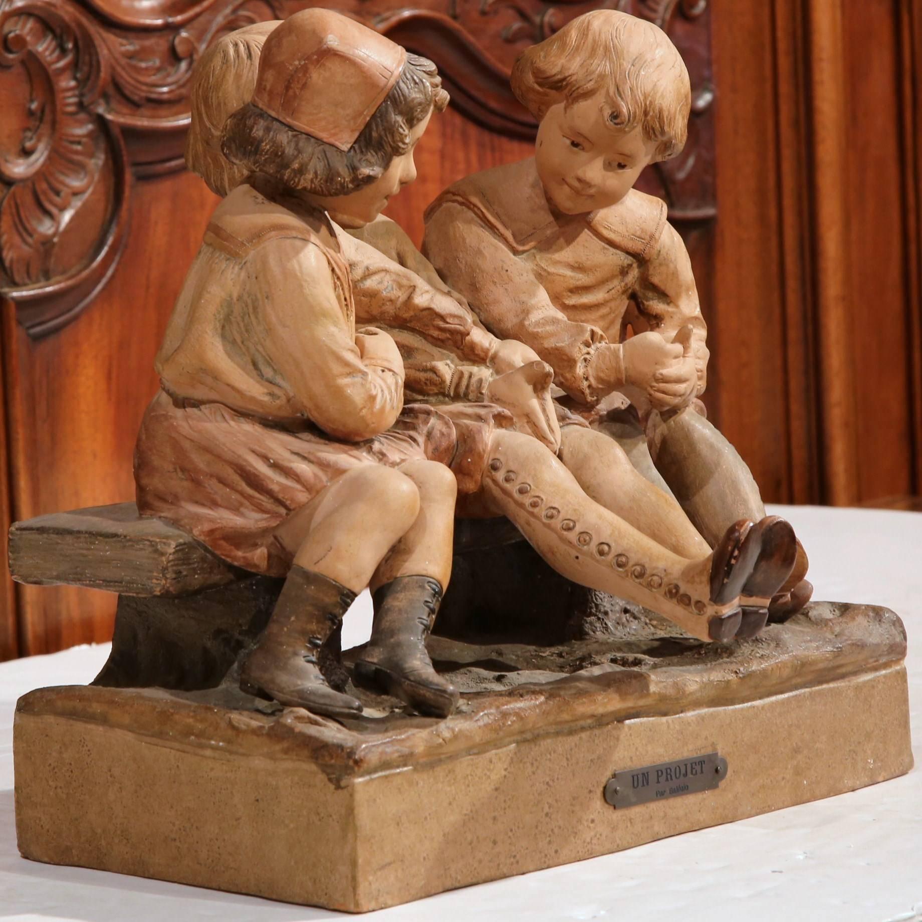 Crafted in France, circa 1880, the antique clay composition features three cheerful children in traditional clothing and boots; they are sitting on a bench, laughing and talking with each other. This work of art has beautiful detailed work with