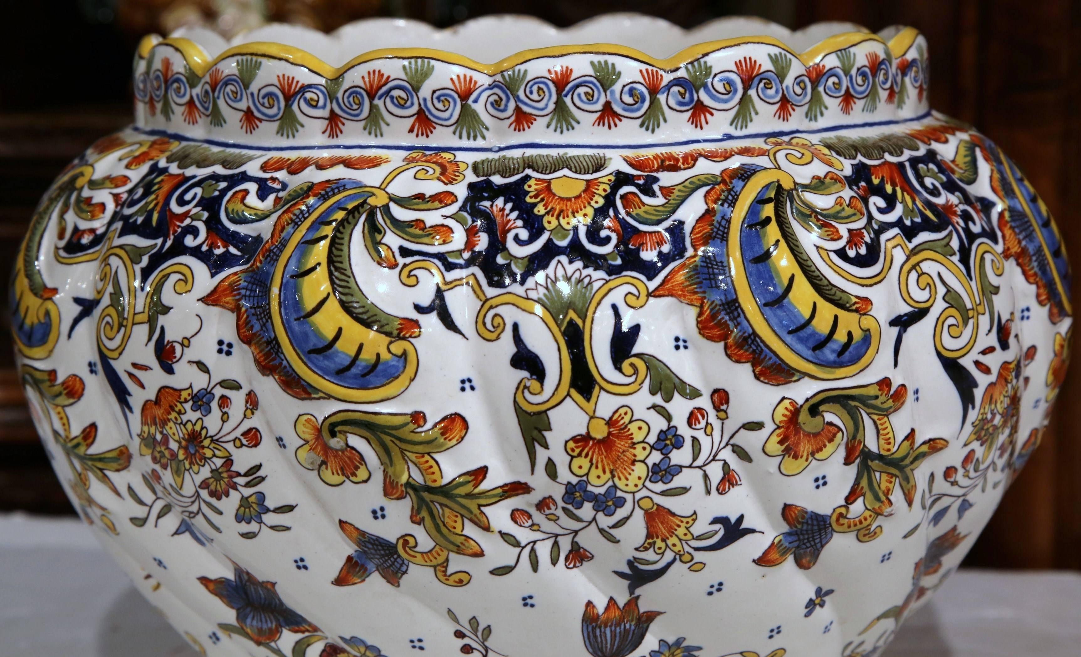 This large colorful, hand-painted jardinière was sculpted in Rouen, France, circa 1920. This ceramic antique planter has a curly, scalloped shape at the rim, and sits on eight small feet. The traditional pot features floral motifs in a blue, yellow,