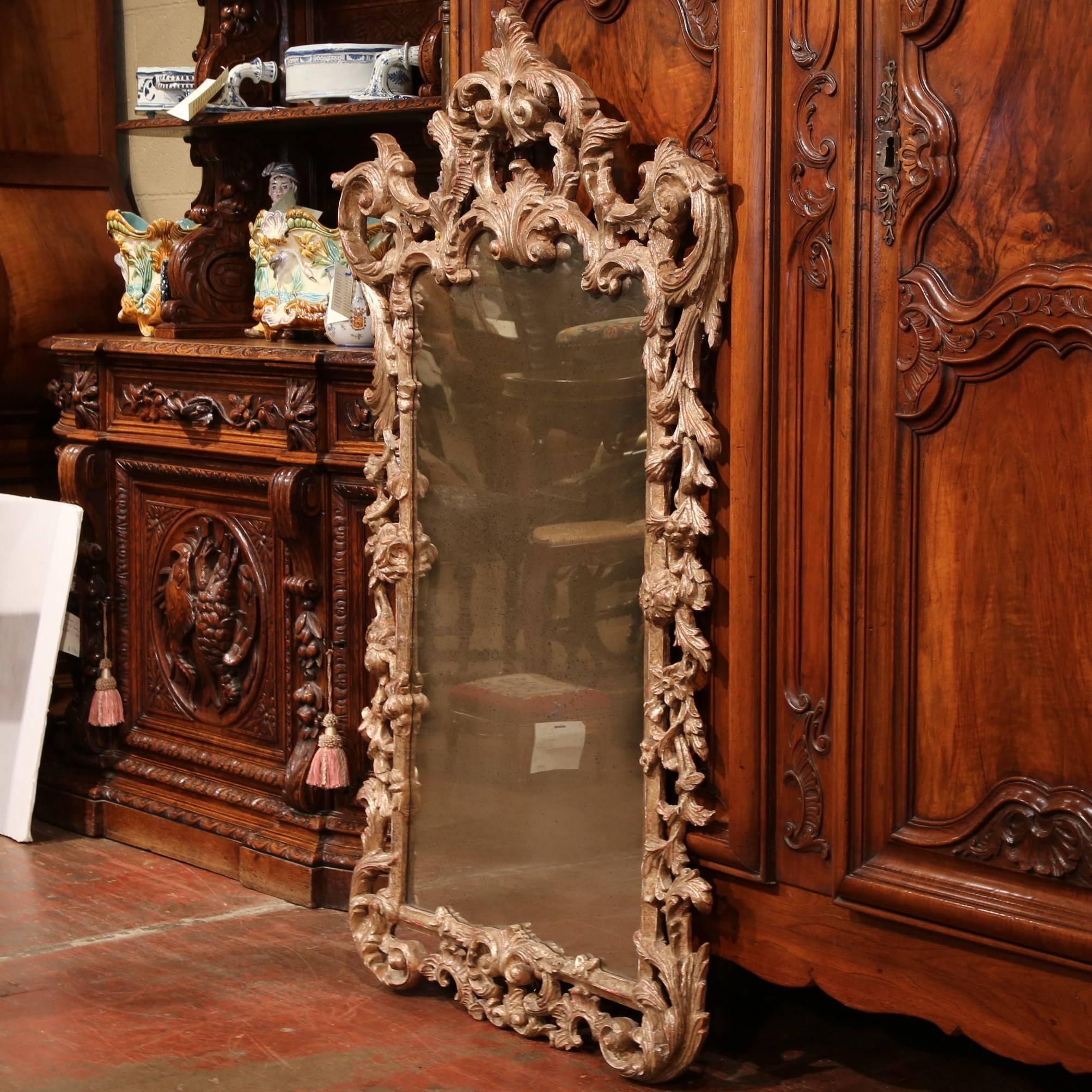 This ornate and elegant carved wall mirror was crafted in Italy, circa 1960. The silver leaf frame features hand carved scroll motifs with floral and leaf decor and is embellished with a smoked mirrored glass. The Rococo mirror is in excellent