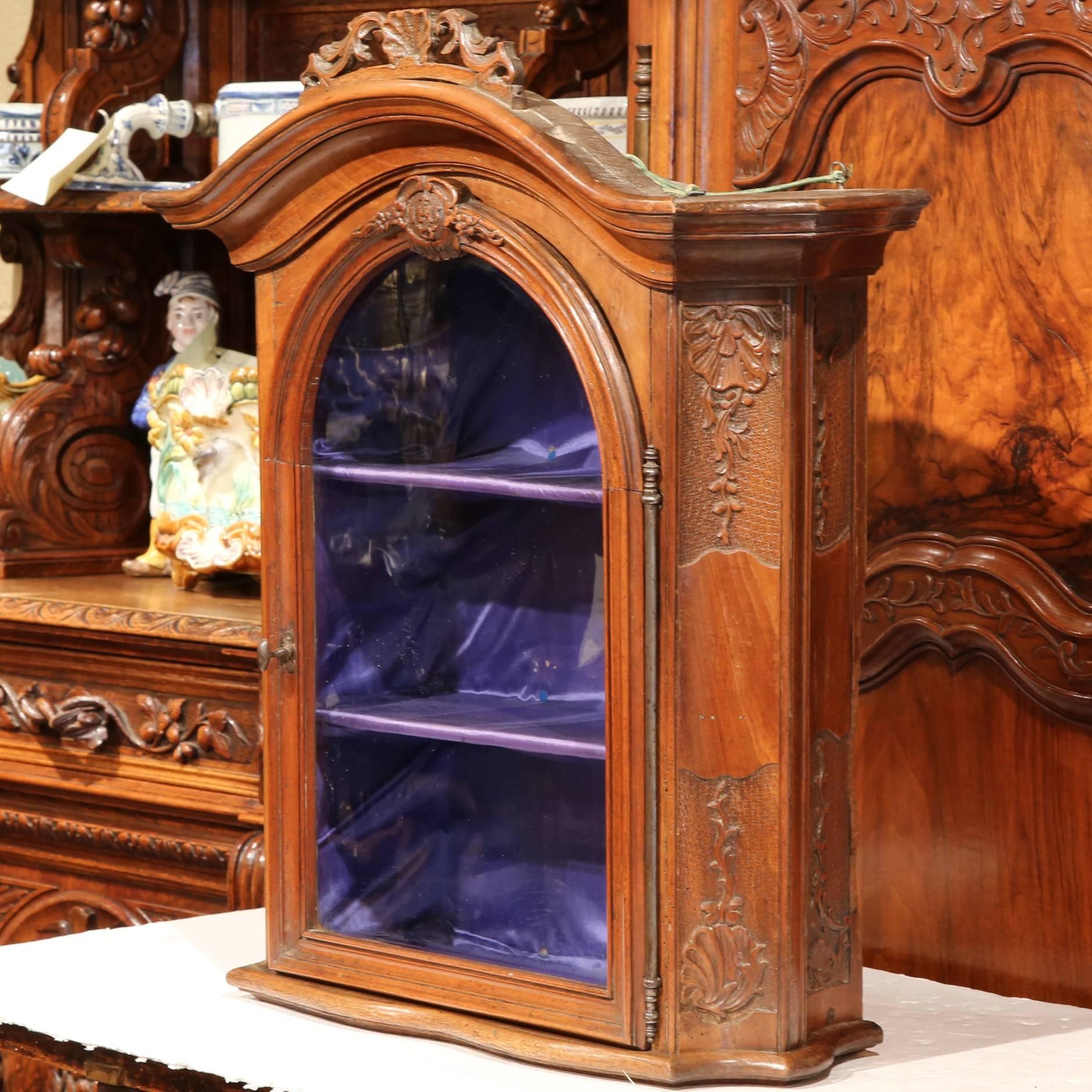 Elegant and narrow antique hanging vitrine from France, circa 1780; with fine carving on both sides and on top of the door, nicely shaped bonnet top, original hardware and glass. Removable blue silk inside. Beautiful and rich patina, excellent