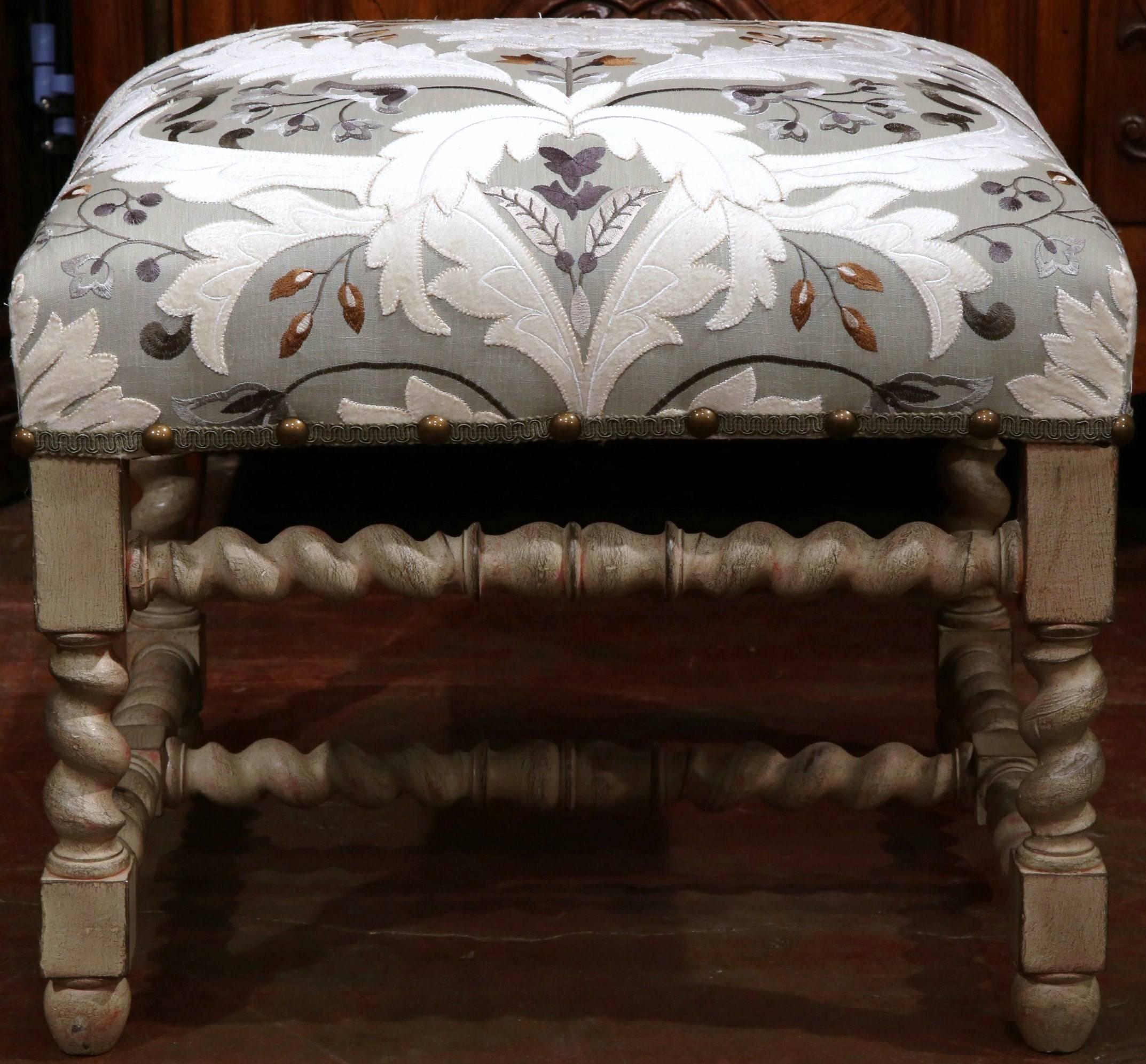 This large, painted stool was crafted in France, circa 1920. Created in the Louis XIII style, this piece has ornate barley twist carved legs with stretcher. The square stool has been reupholstered with embroidered, contemporary fabric decorated with