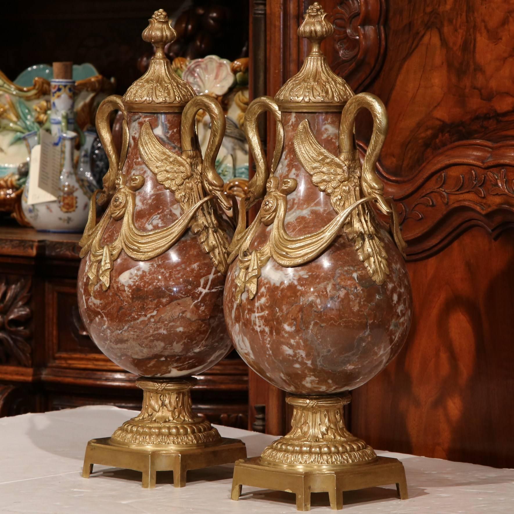 This fine pair of marble and bronze cassolettes was created in France, circa 1870. The unique, beautiful urns are decorated with ornate bronze decorations that include swan head handles and dramatic garlands. The pieces have a red marble and white