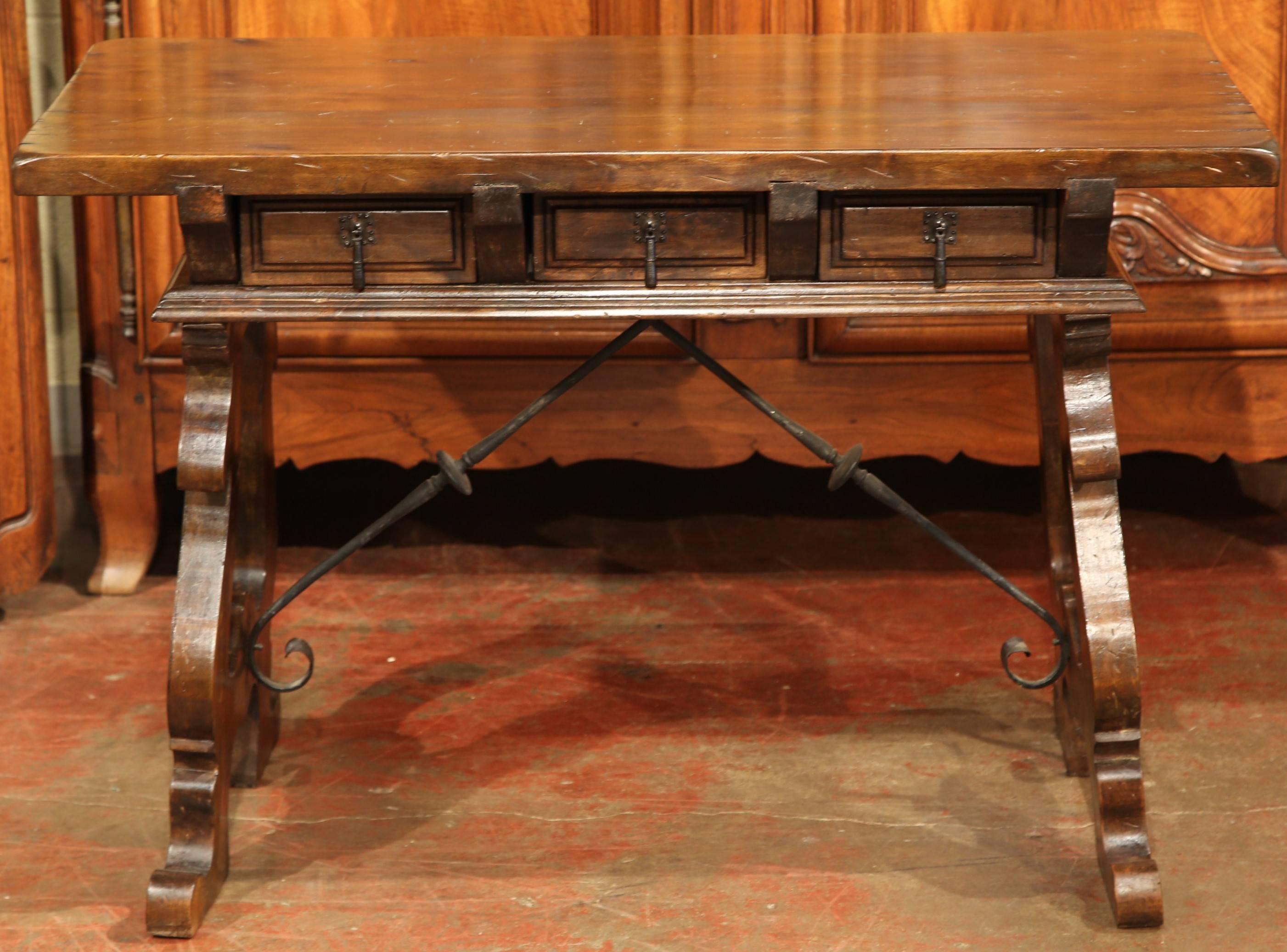 This fine fruitwood writing table was carved in Spain, circa 1920. The small table has a pair of drawers across the front and two carved legs connected with a prominent iron stretcher. This small desk could also be used as an end or side table in a