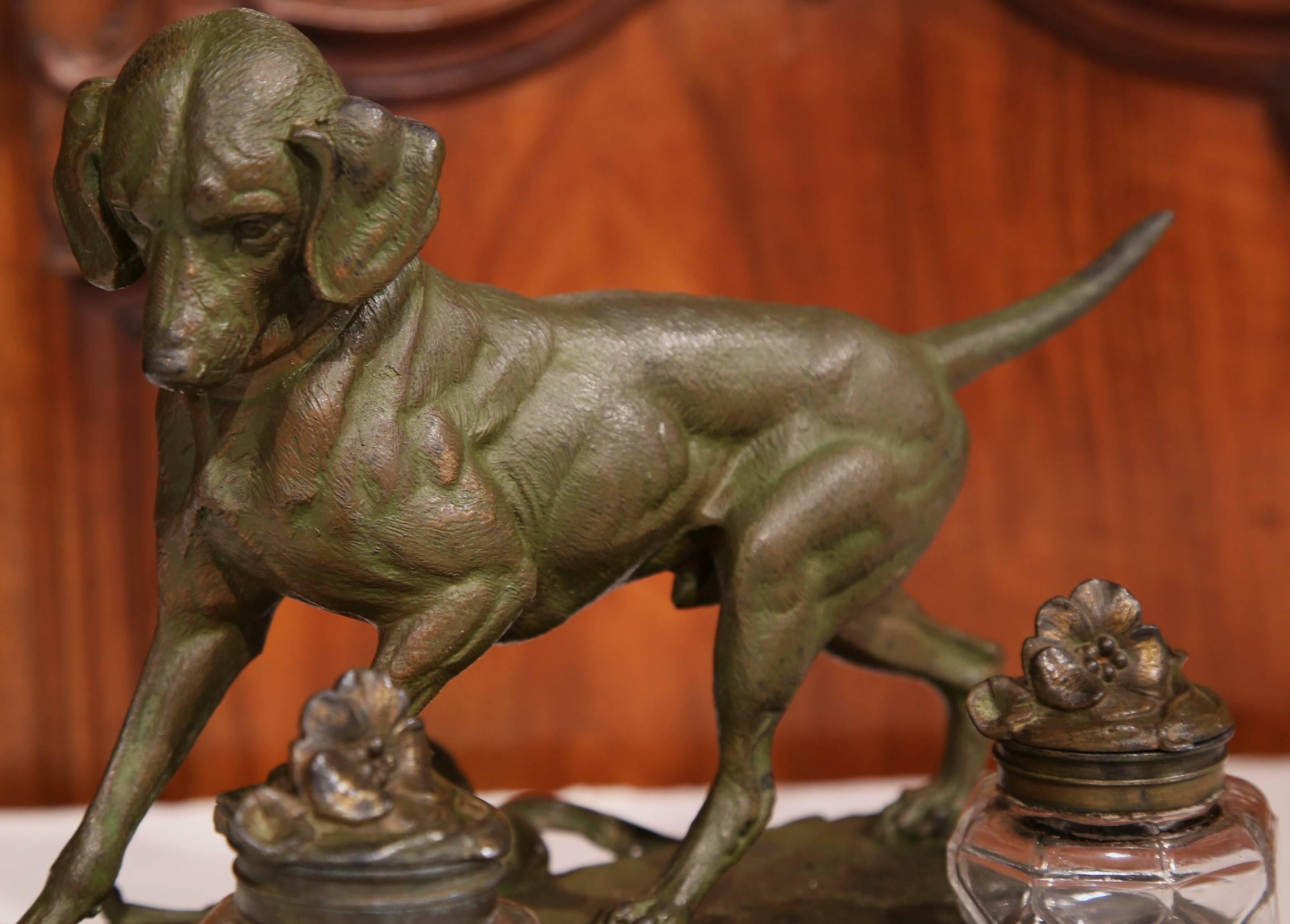 Decorate your desk with this fine, antique inkwell from France, circa 1870. The patinated spelter piece is embellished with a finely sculpted hunting dog, and has two glass ink holders with flower decorated lids. The piece is signed and is in