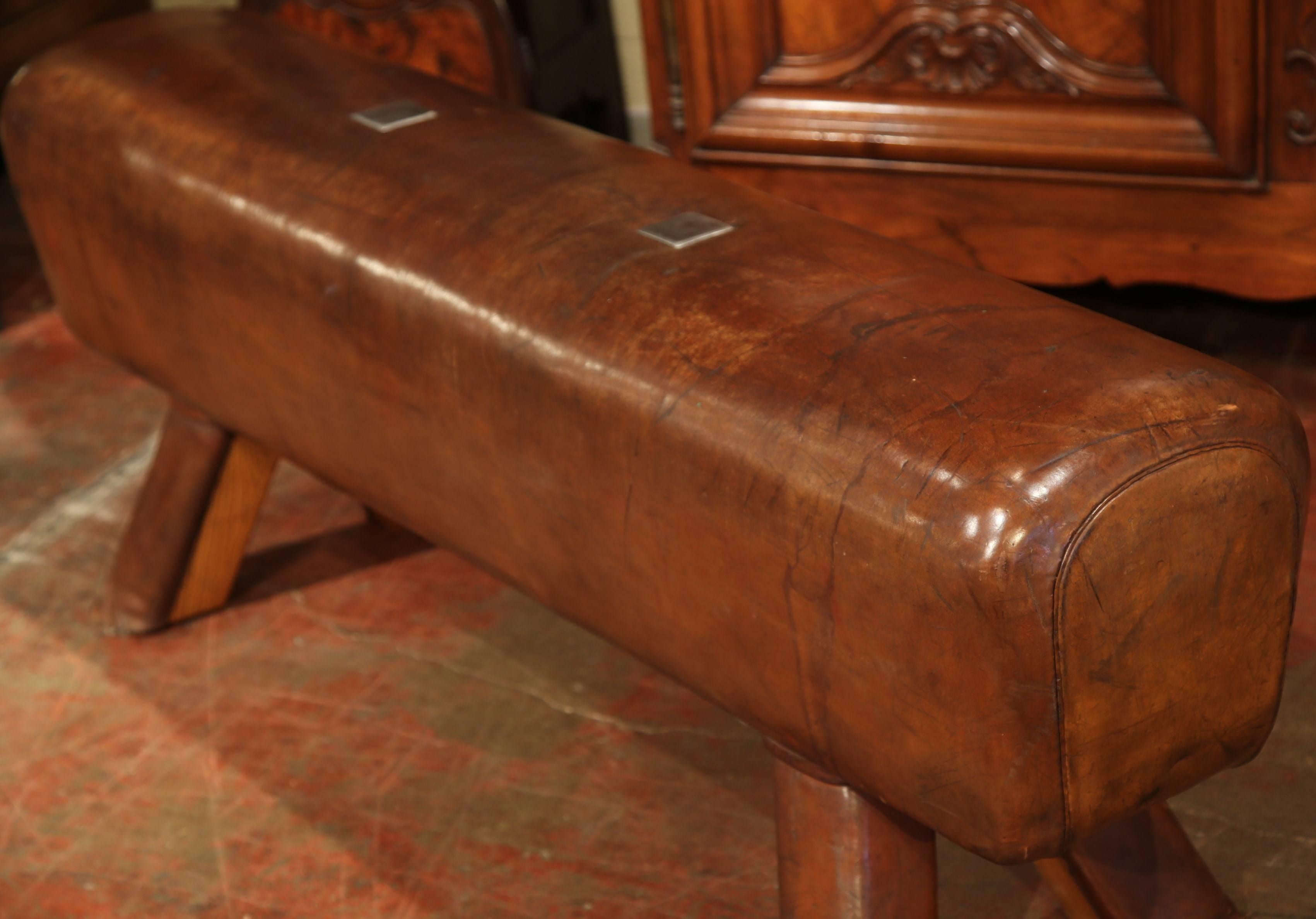 This antique, leather pommel horse bench features original leather and was crafted in the Czech Republic circa 1920. The rustic piece has wooden legs covered in leather and custom steel plates have been added to cover the location of the original