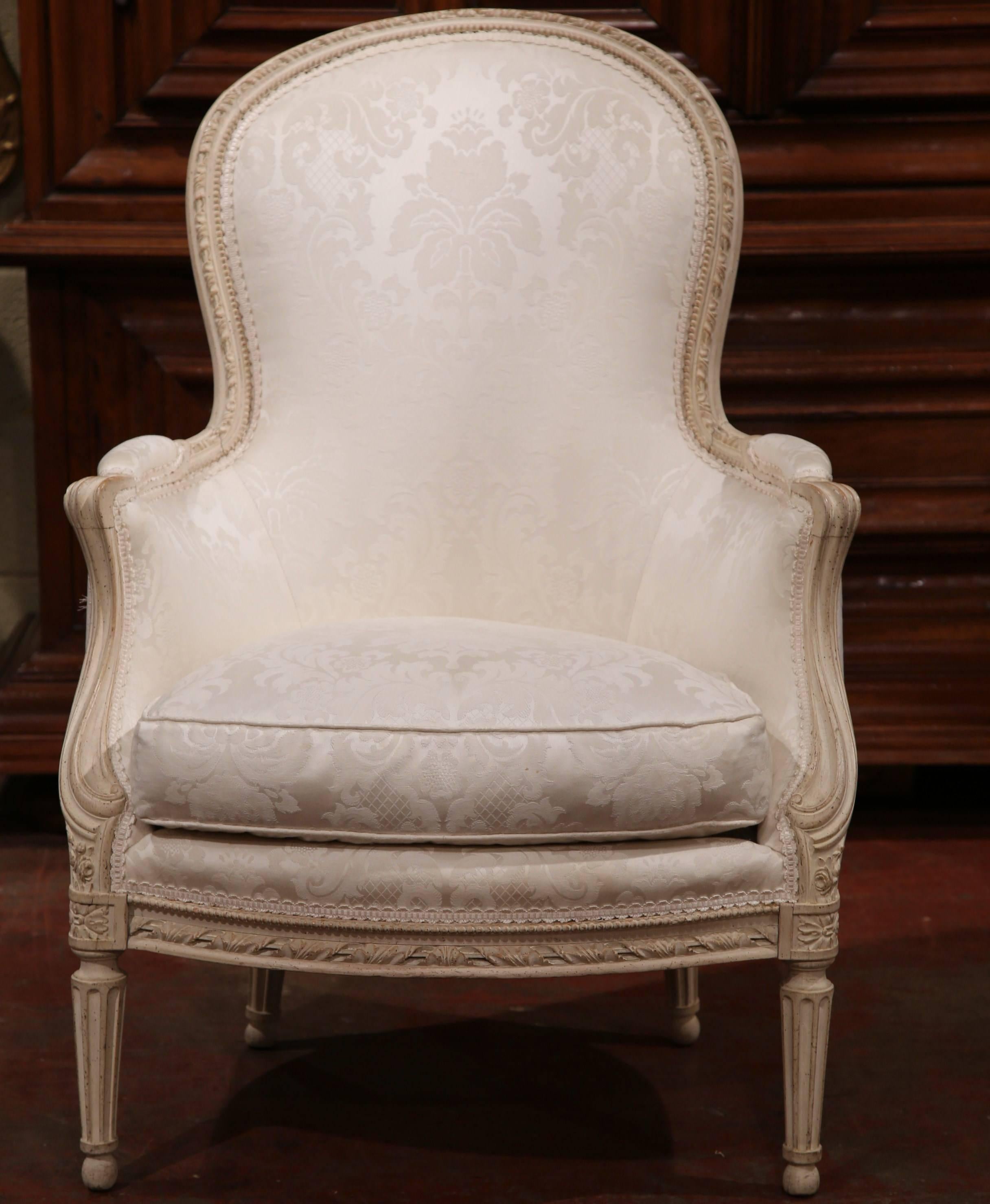 These elegant painted antique bergères were crafted in France, circa 1960. Each comfortable armchair features beautiful hand carved decor, including a rounded and arched back, curved armrests, tapered and fluted legs, and a removable feather filled