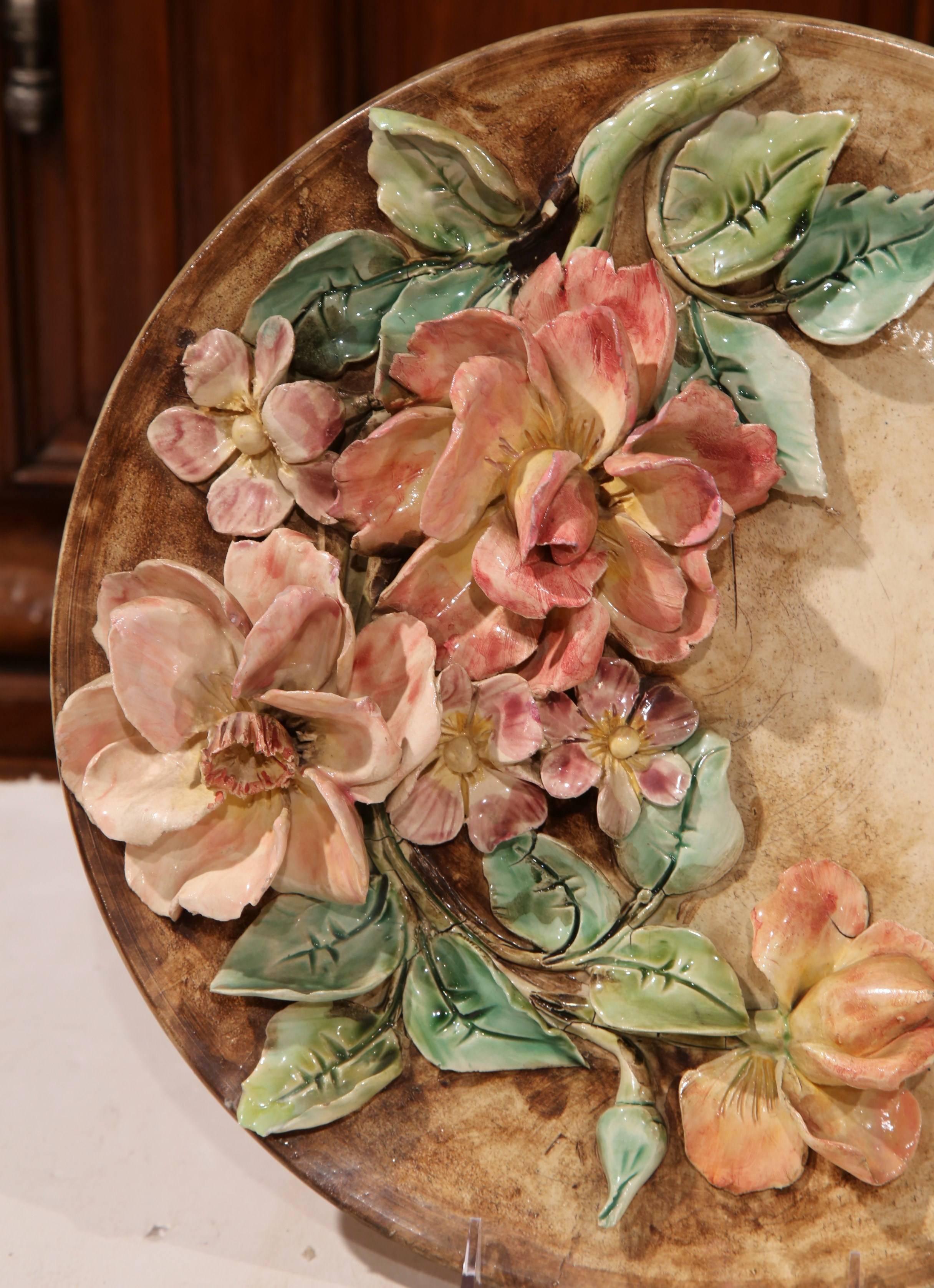Ajoutez de la couleur à votre salle à manger ou à votre cuisine avec ce plat ancien en majolique, datant des années 1880, en France. La grande assiette est ornée de fleurs finement sculptées dans une palette rose, rouge et verte. Au dos, le plateau