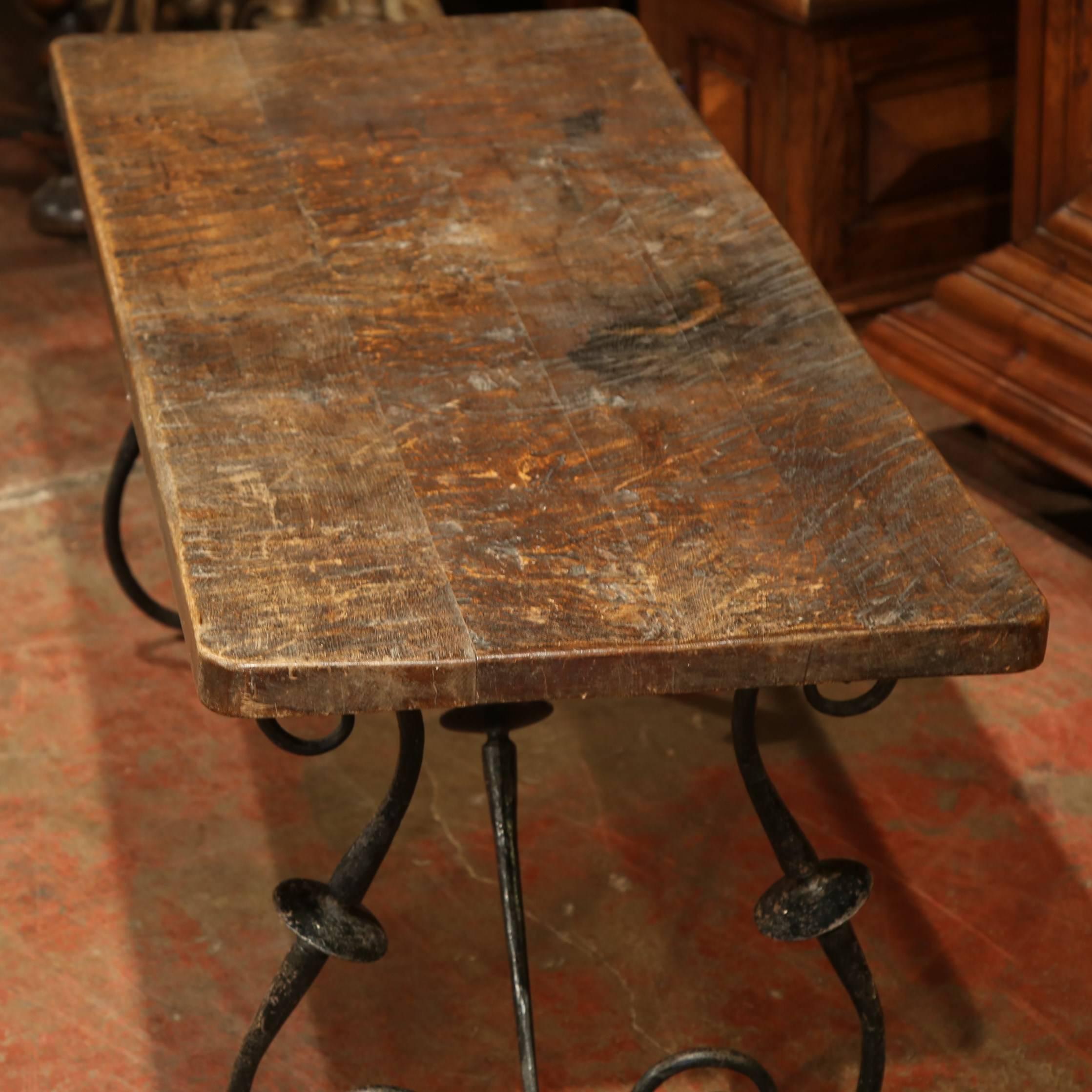 This elegant, antique coffee table was created in Spain, circa 1890. The table features a wooden, walnut tabletop, and scrolled, iron legs connected with an iron stretcher. The top is unique, hand-cut with a saw or ax from one piece of solid wood.