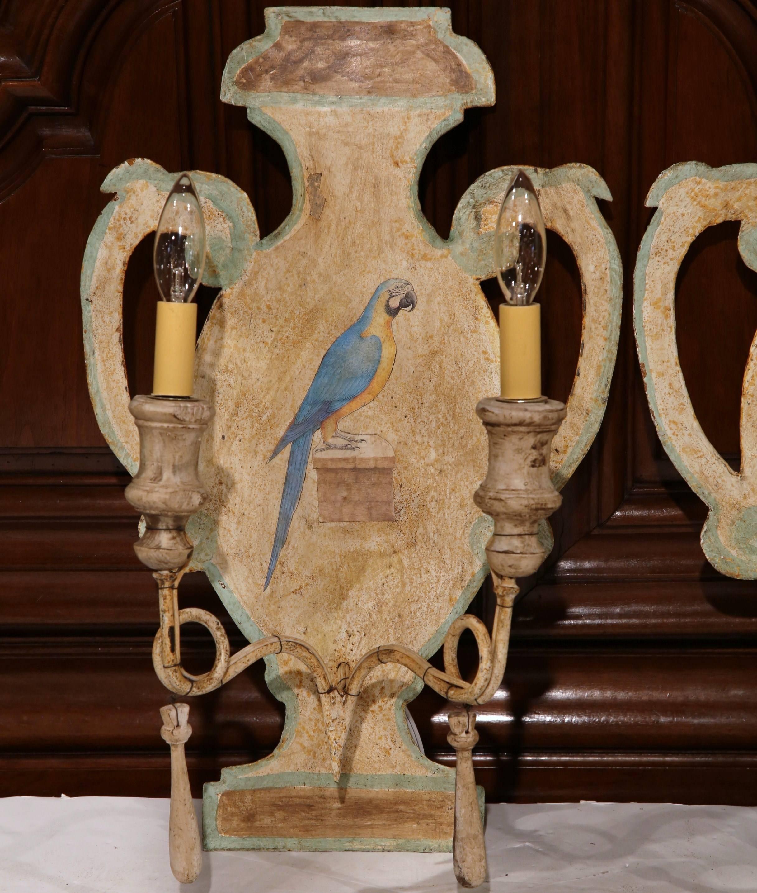 Decorate an entryway or living room with this colorful pair of tole sconces from France, circa 1960. Each wall light is shaped like a vase with handles and features a hand-painted, blue parrot in the center. Both arms have wood bobeches and finials,