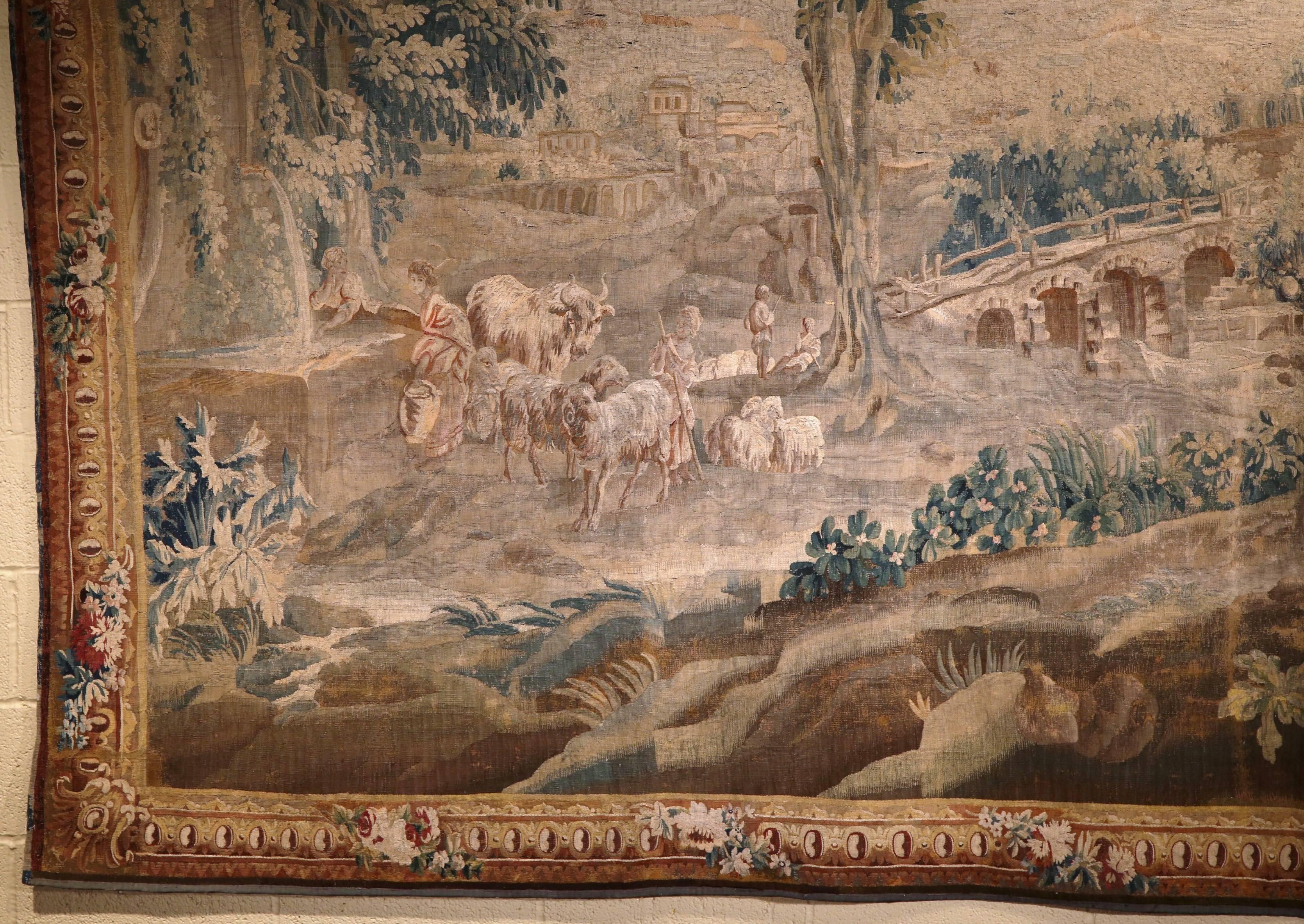 Make a statement in your home with this antique Aubusson tapestry from France, circa 1740. In the style of Boucher, this piece depicts a pastoral scene with a shepherd, sheep, a chateau and bridge in the background, and a trio of amorous courtly