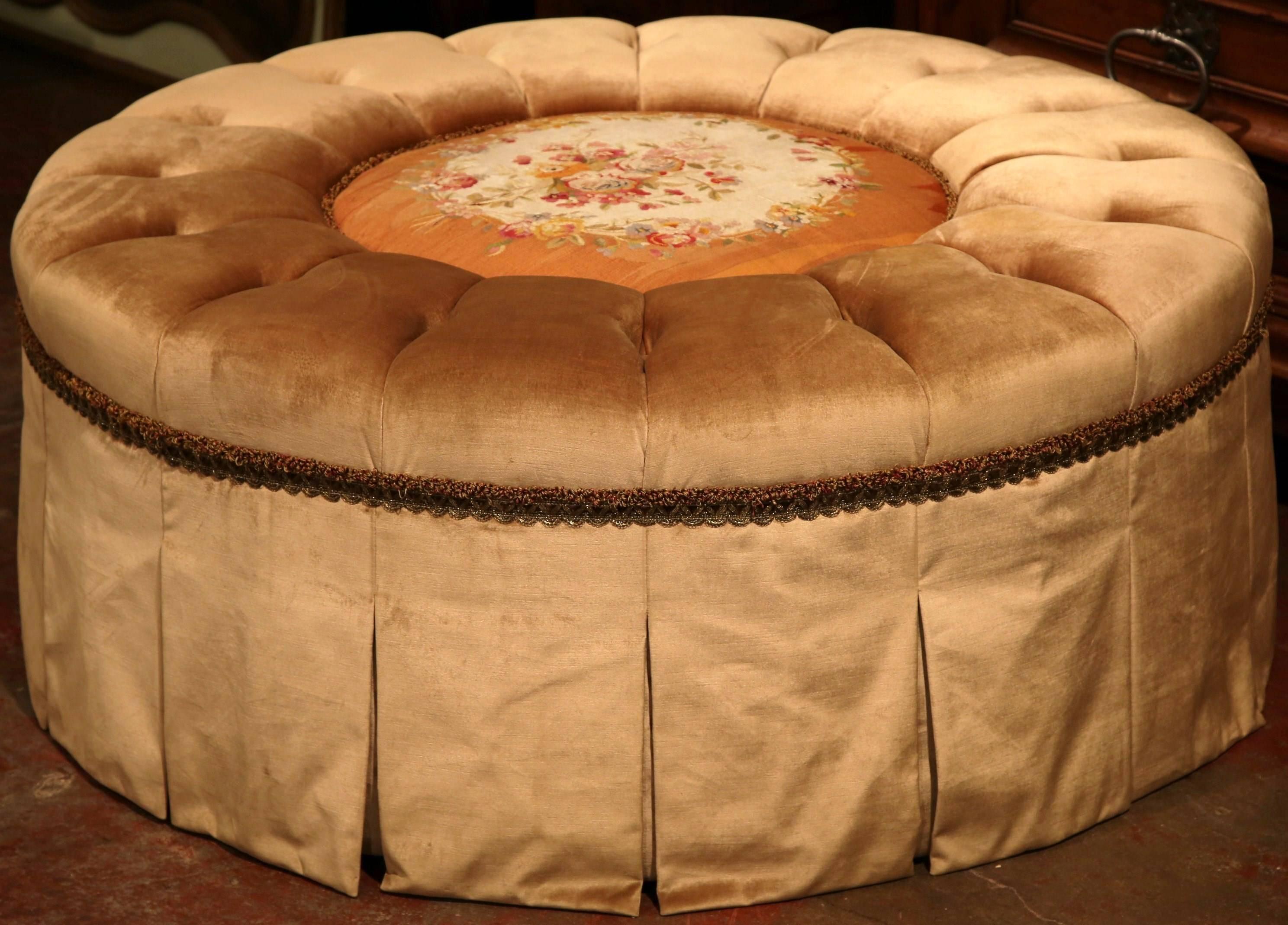Create extra sitting or surface space in your living room with this large stool or coffee table. Created in France, this round ottoman features a colorful, floral Aubusson tapestry in the centre. This piece is in a neutral beige, golden palette and
