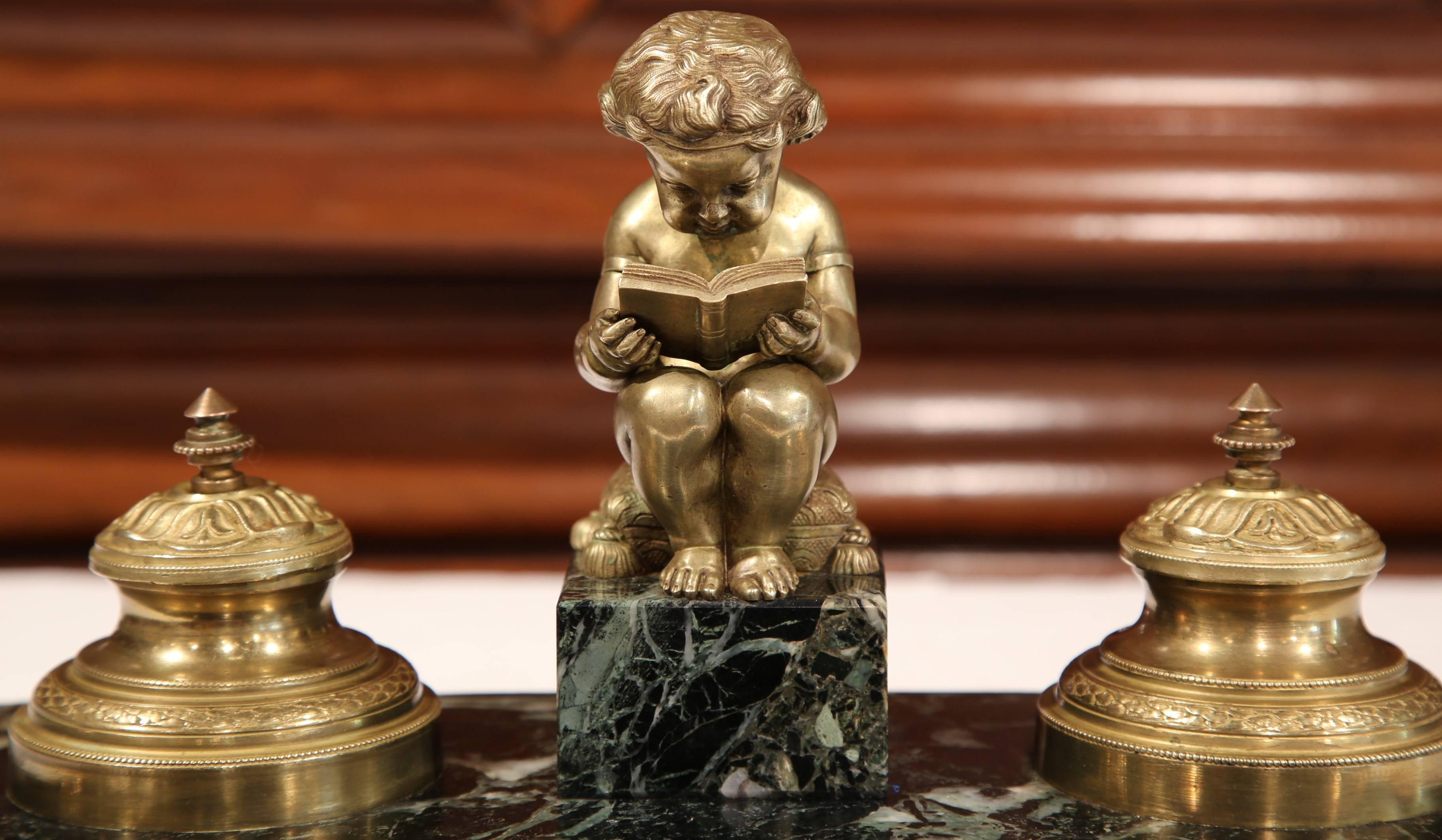 Embellish your desk with antique flair with this fine inkwell from France. Crafted, circa 1870, the symmetrical inkwell features a bronze young boy sitting on a cushion while reading a book. On either side of the cherub, are two bronze inkwells with