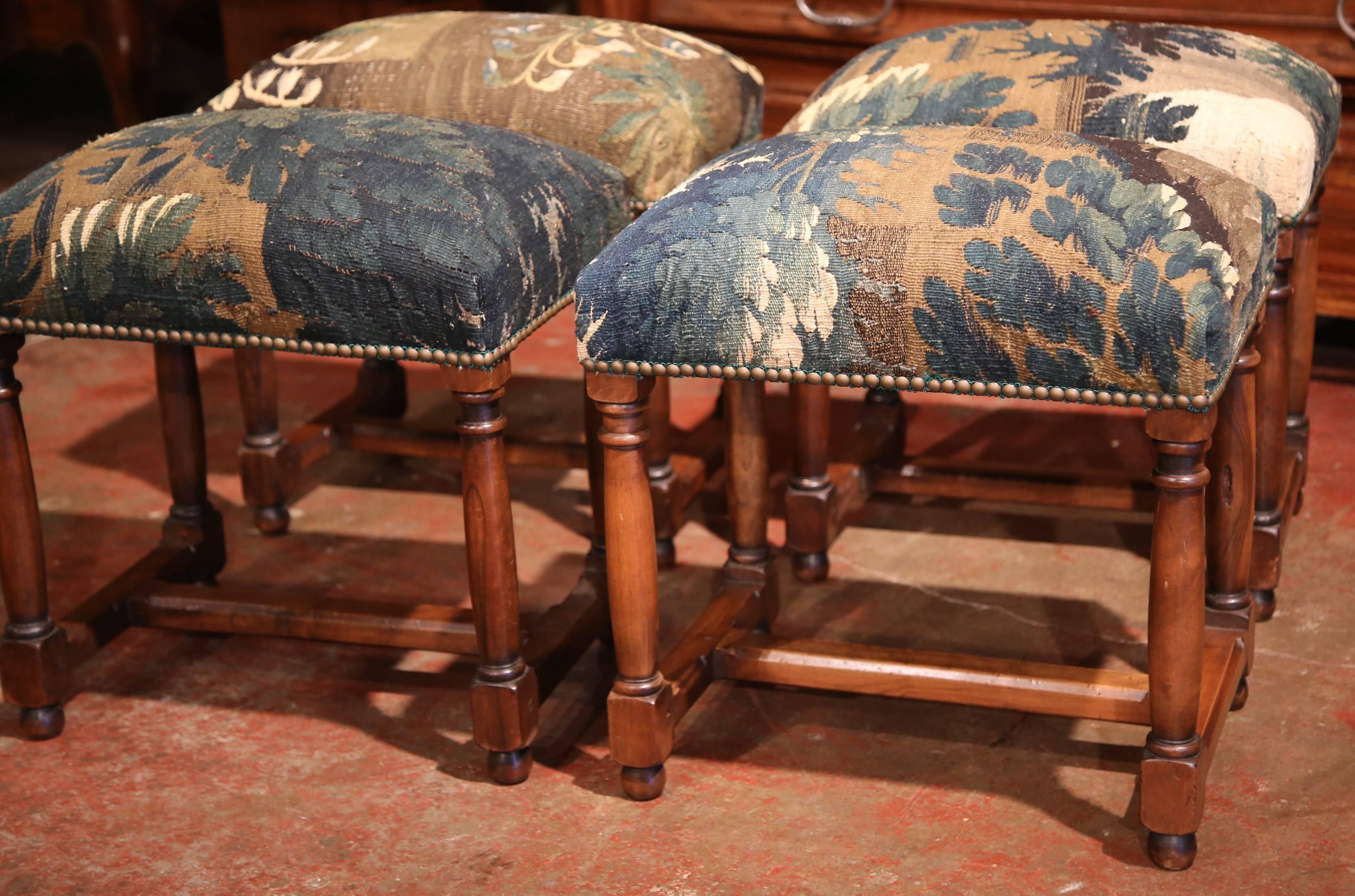 This exceptional suite of four Louis XIII fruitwood stools was crafted in Southern France, circa 1890. All four antique pieces are upholstered with 19th century Aubusson verdure tapestry in a classic brown, blue, green and beige color palette. The