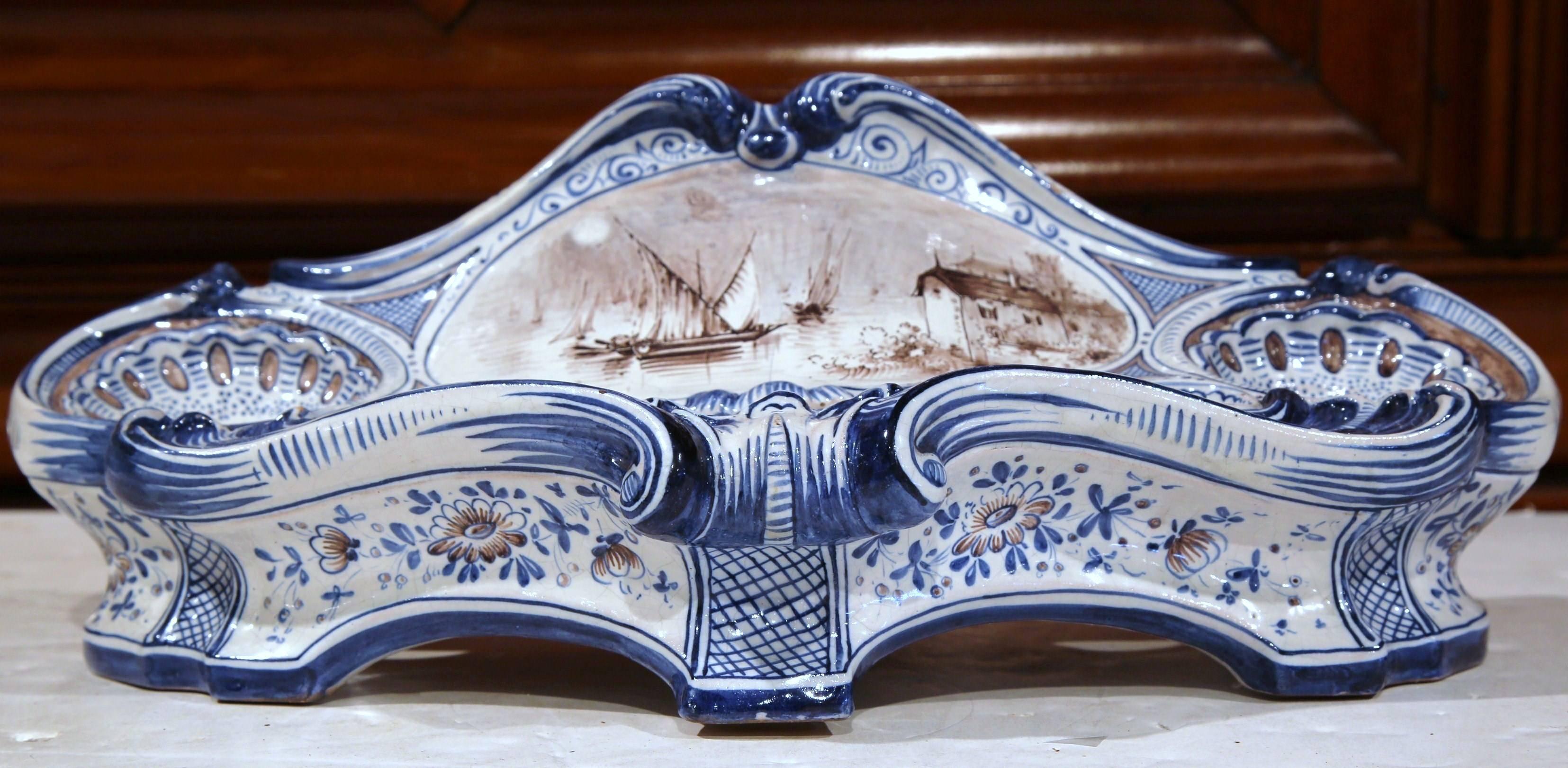 This uniquely shaped ceramic inkwell was sculpted in France, circa 1880. The cartouche-shaped desk essential features a hand painted black and white center medallion with sailboats, farm house and blue floral motifs. The blue and white palette along