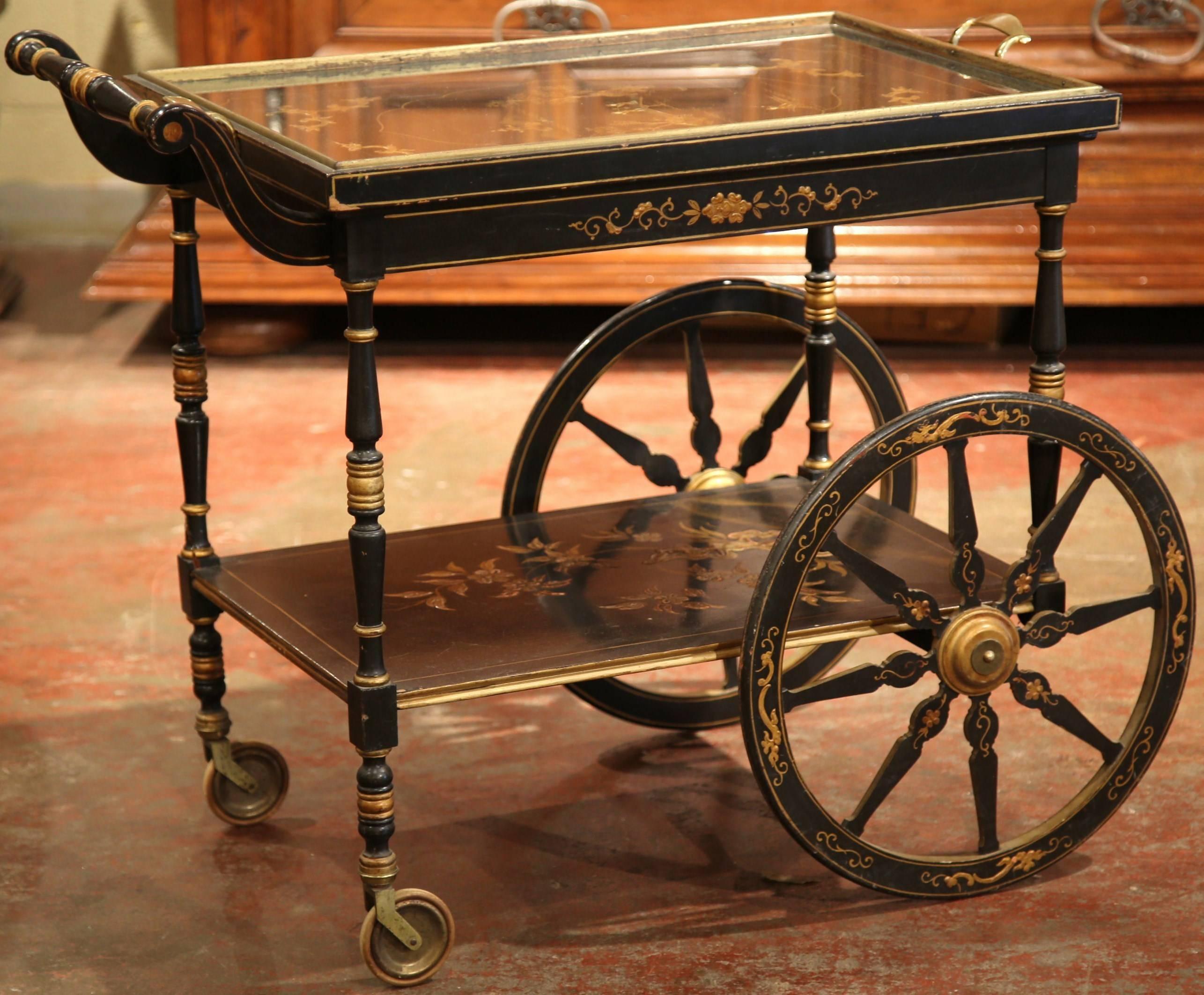 This fine wooden tea cart was created in France, circa 1920.The cart is on wheels and is painted black with chinoiserie decorative embellishments including hand-painted flowers and gilt accents. The cart features a removable glass tray with brass