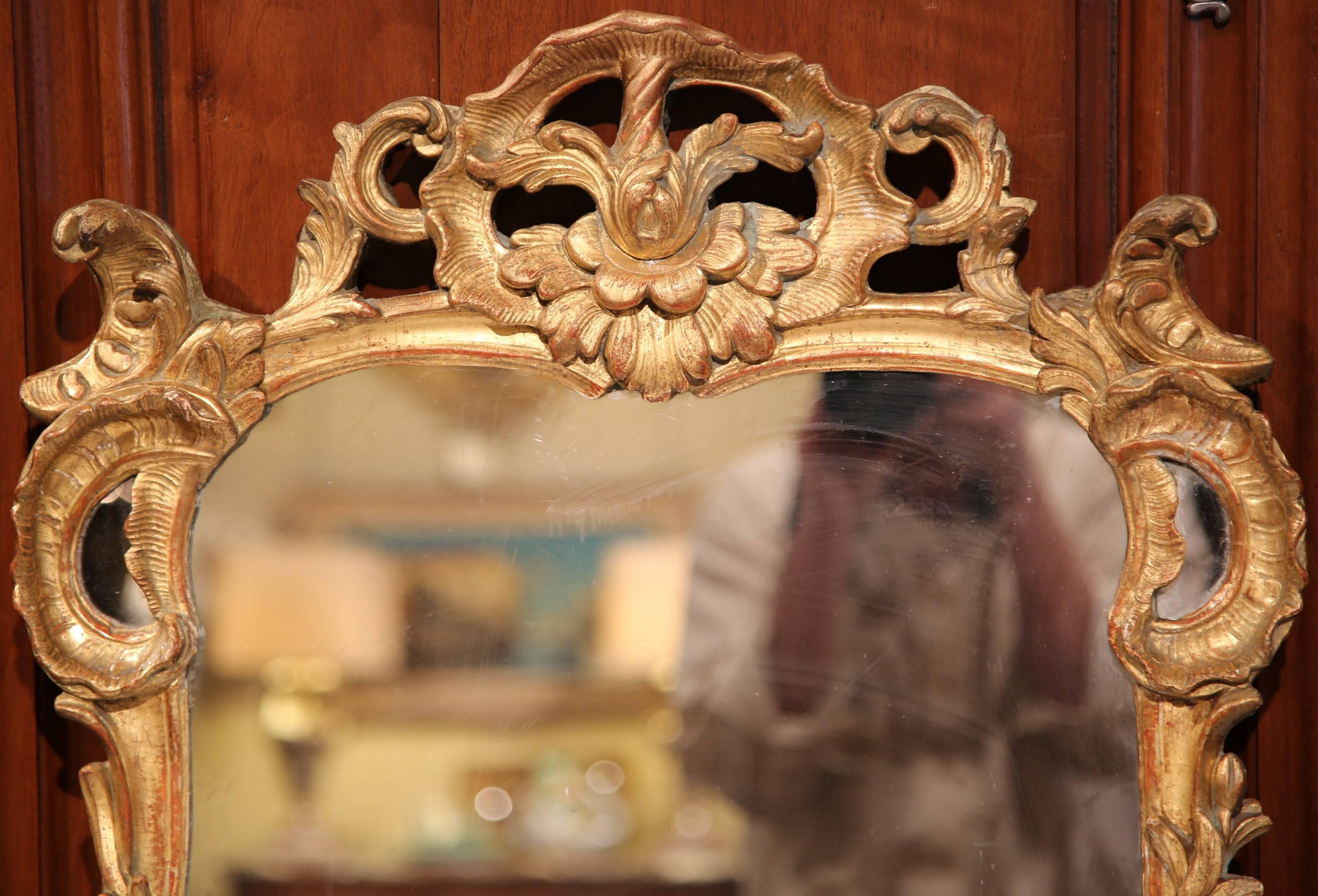 This elegant antique mirror was crafted in Southern France, circa 1780. The rectangular mirror features a nicely carved pediment at the top, has delicate scrolls and flowers and on either side there are carvings that resemble tree branches. The