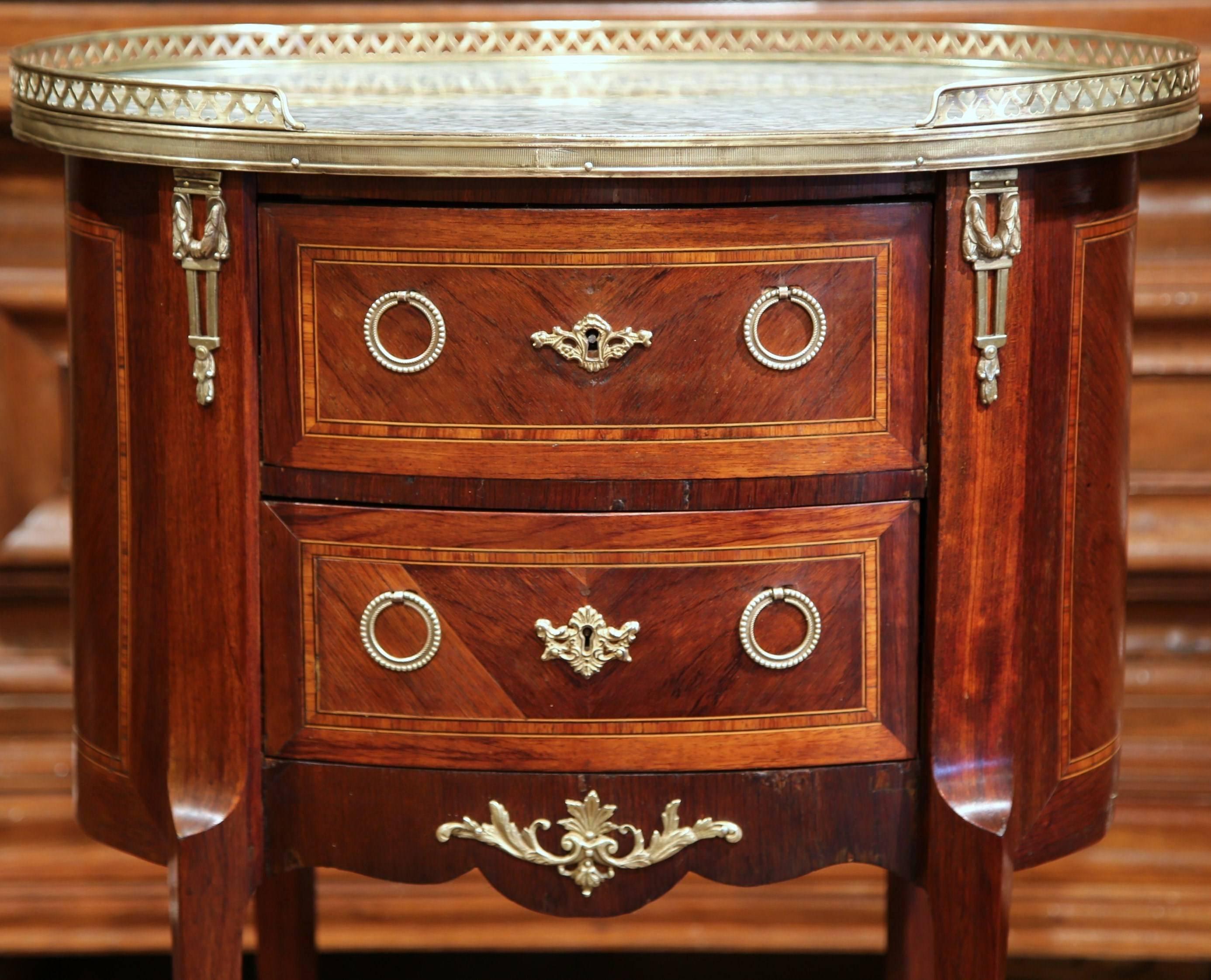 This small, antique oval chest of drawers was crafted in Paris, France, circa 1870. The elegant commode has its original grey marble top with a decorative brass gallery around the periphery. There is beautiful marquetry work on the front and sides,