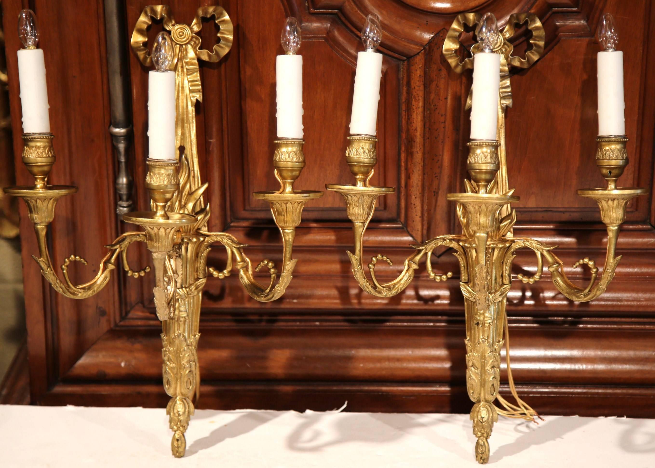 This elegant pair of antique bronze sconces was created in Versailles, France, circa 1870. The light fixtures each have three arms, intricate bronze work and decorated with a traditional Louis XVI stylized bow ribbon at the top. The wall lighting is