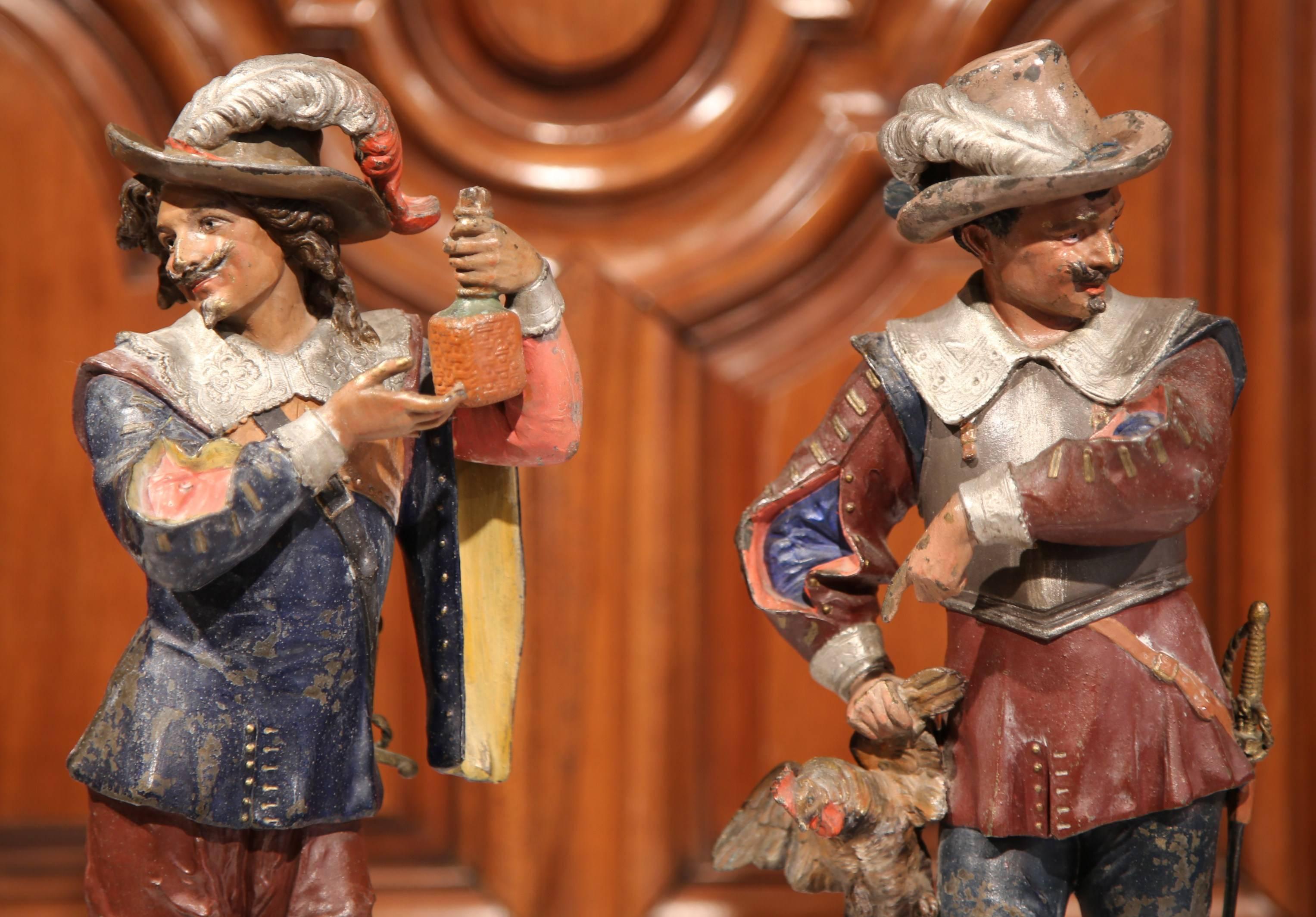 Decorate a mantel or a shelf with these elegant and colorful antique statues. Crafted in Southern France, circa 1870, each metal sculpture features a realistic, expressive musketeer in traditional outfits; one man is pointing at the rooster he just