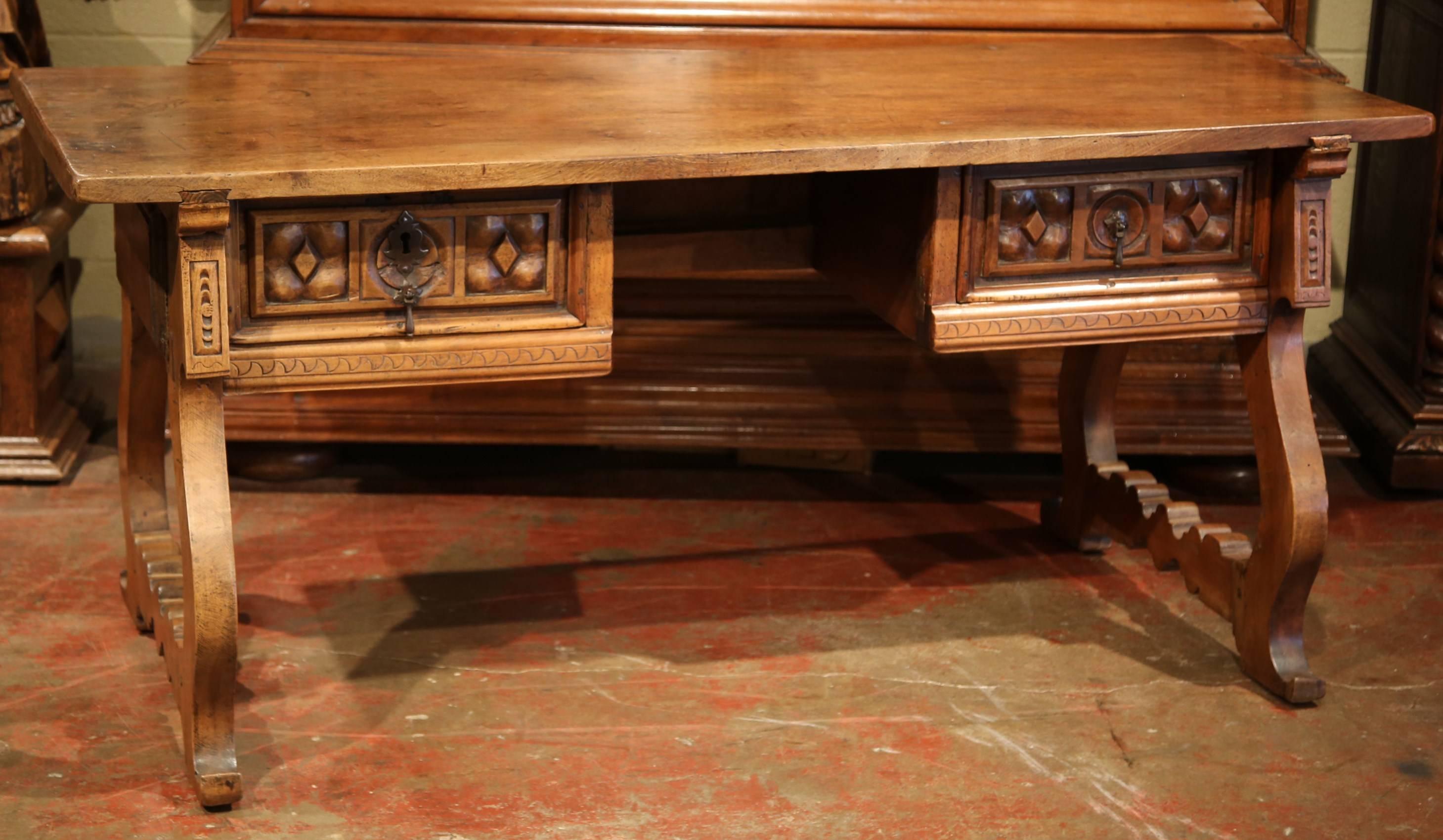 This elegant, antique fruitwood desk was carved in Spain, circa 1860. The tabletop is made of one single plank with two carved drawers, original iron pulls, lock and key. The desk sits on a pair of carved legs with scrolled feet. Excellent condition
