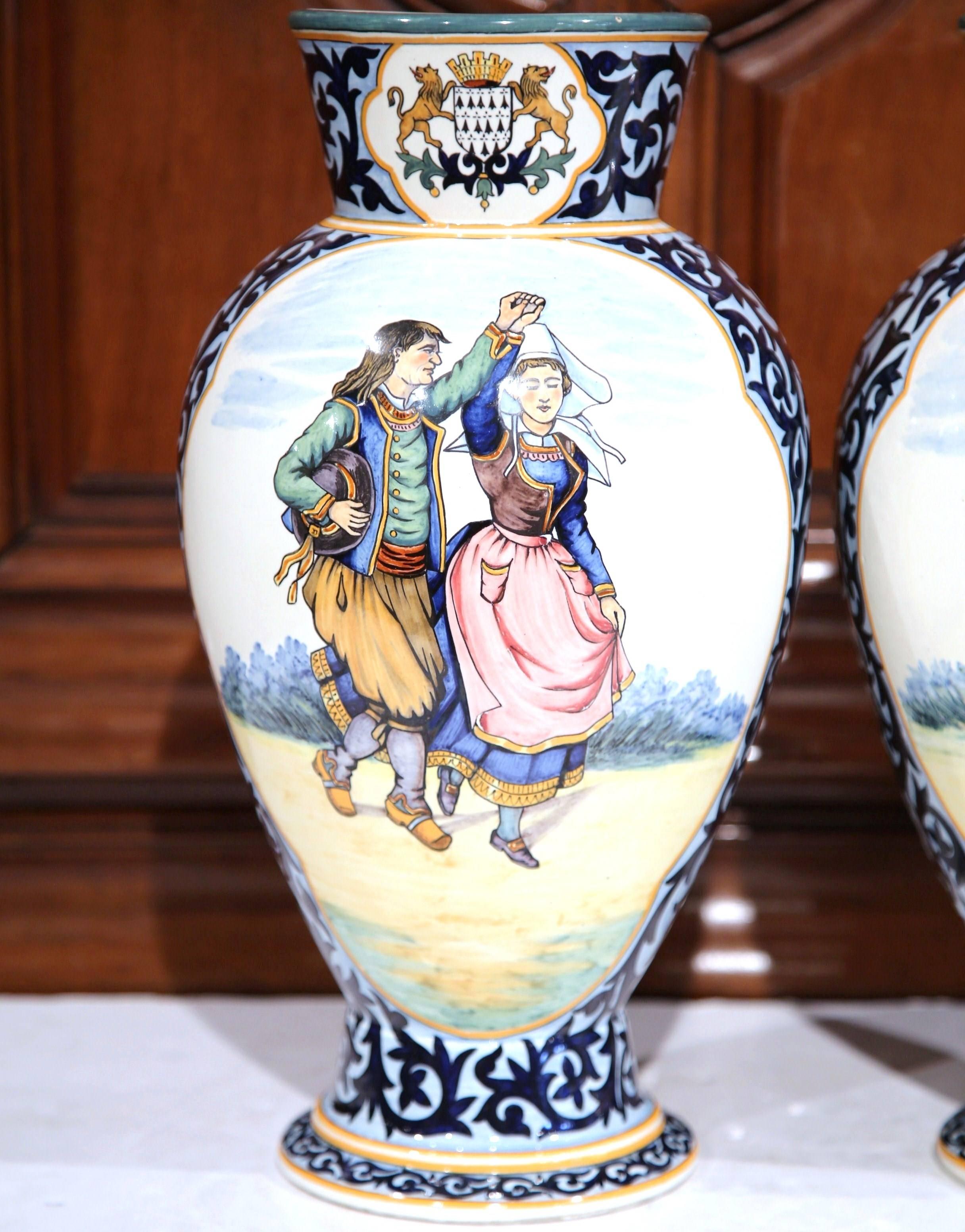 Decorate a mantel or table with this large pair of antique vases. Crafted in Brittany, France, circa 1880, both colorful jars are hand painted with Britons people dressed in traditional outfits, dancing and playing the bagpipe; they are further