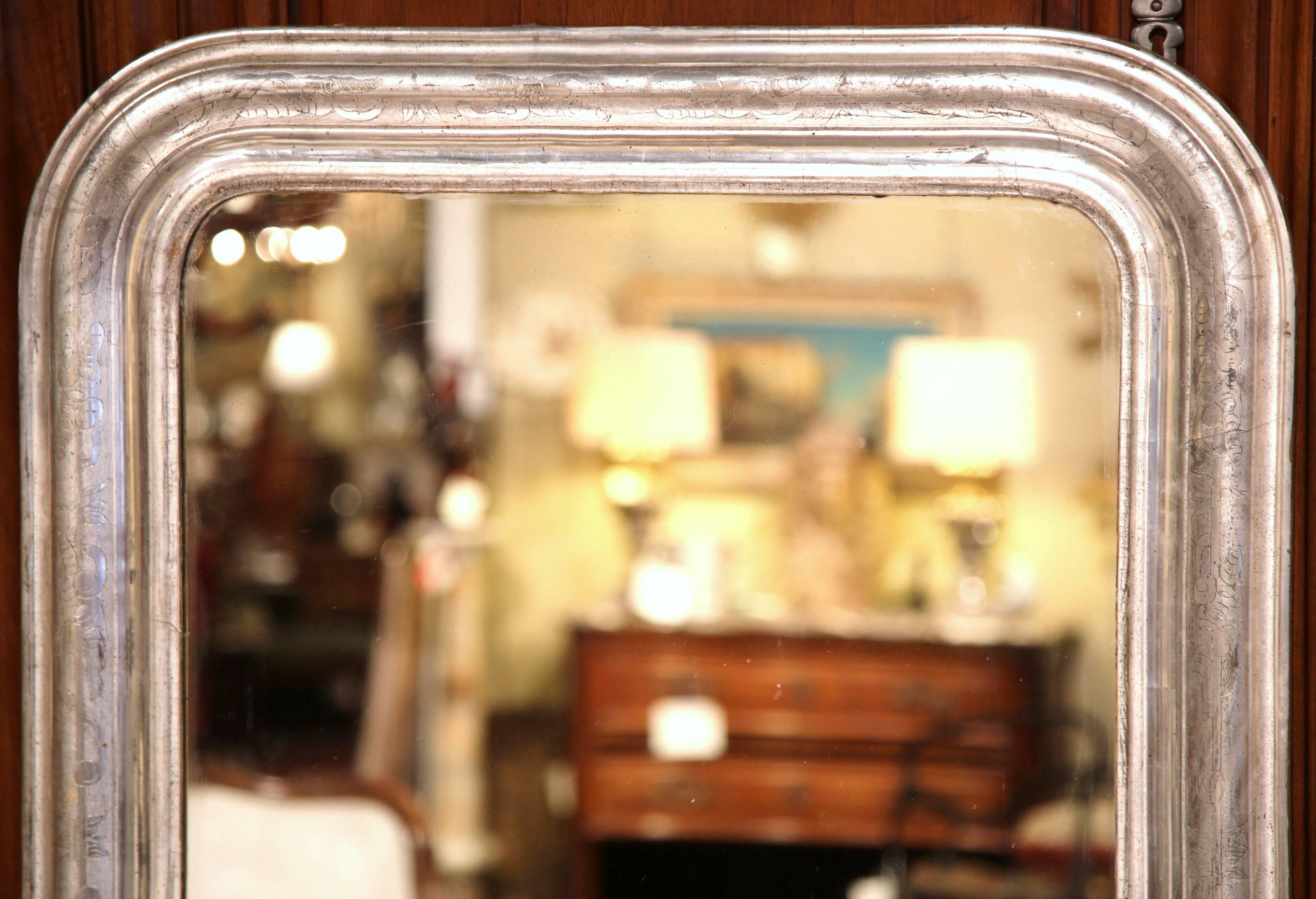 This elegant, antique Louis Philippe mirror was crafted in France, circa 1870. The mirror features discrete engraved floral designs around the frame over the original silver leaf finish. Place the Classic, metallic mirror at the end of a hallway, in