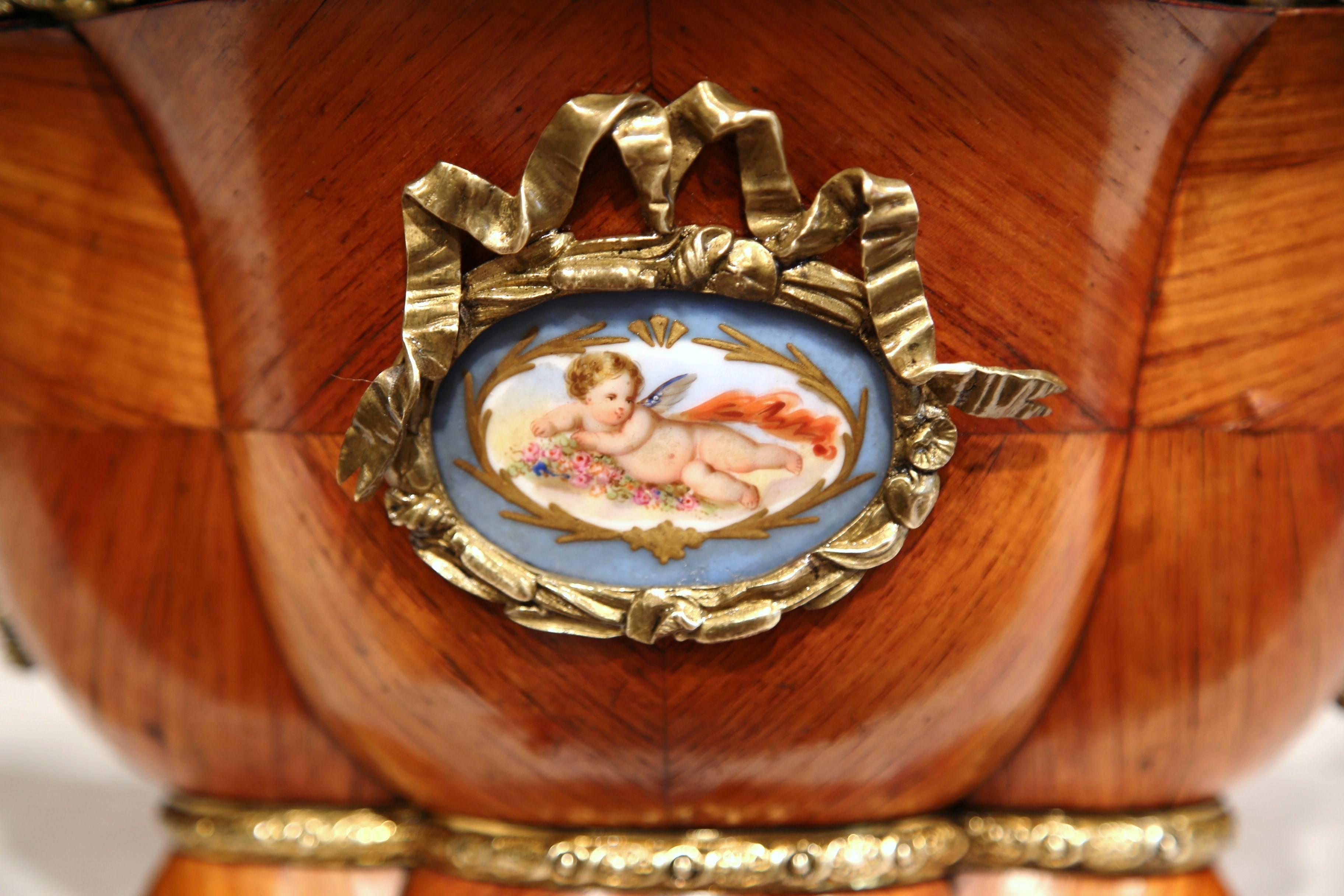 Decorate a table with this elegant antique Louis XVI jardinière. Crafted in Paris, circa 1820, this fruitwood planter features a decorative porcelain plaque on both sides featuring a cherub with wing. The hand painted medallion is further decorated