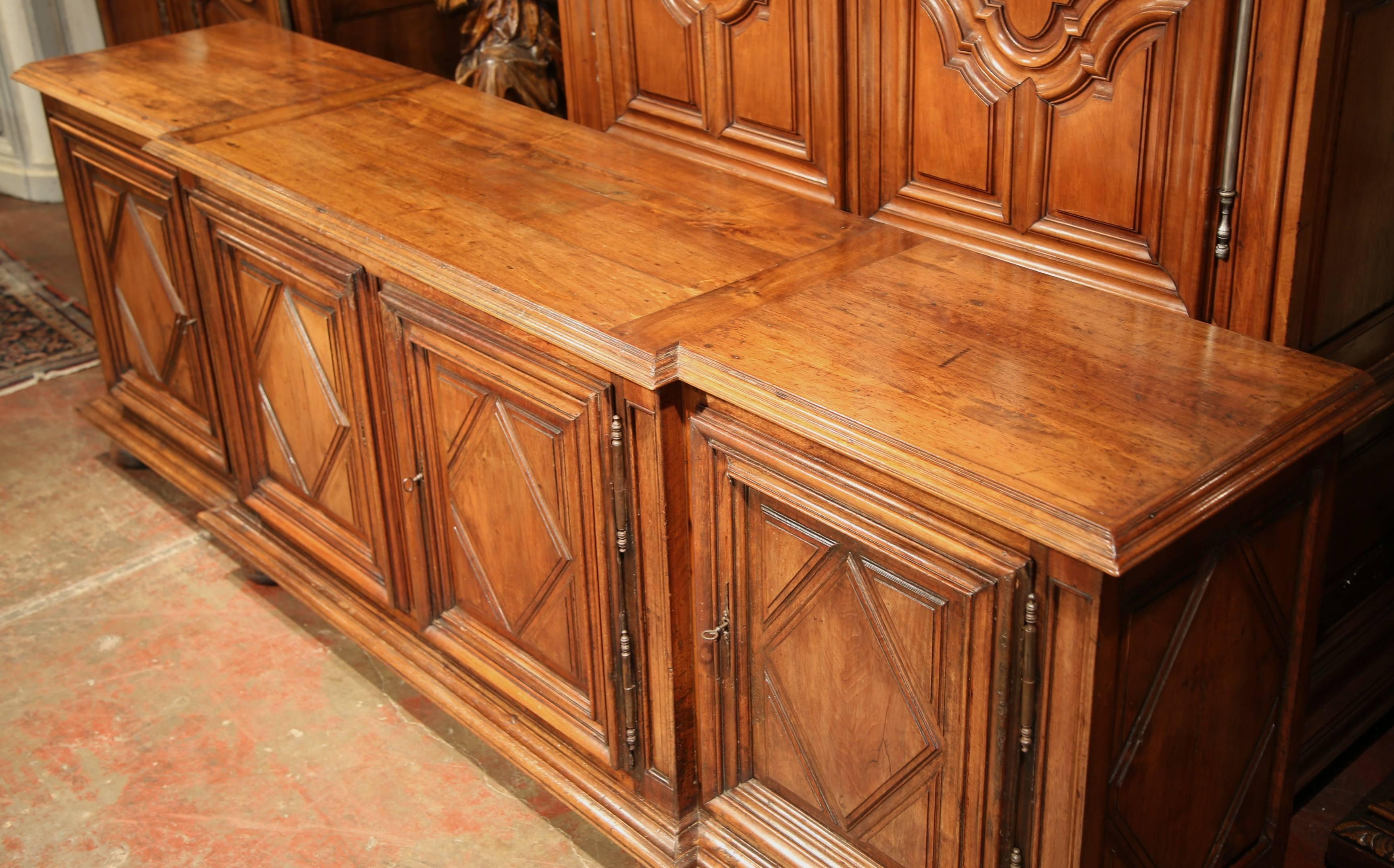 This large, antique fruitwood buffet was carved in the south of France, circa 1820. The long cabinet features four doors with a simple, geometric diamond shape design. The utilitarian piece sits on bun feet and offers ample storage space behind the