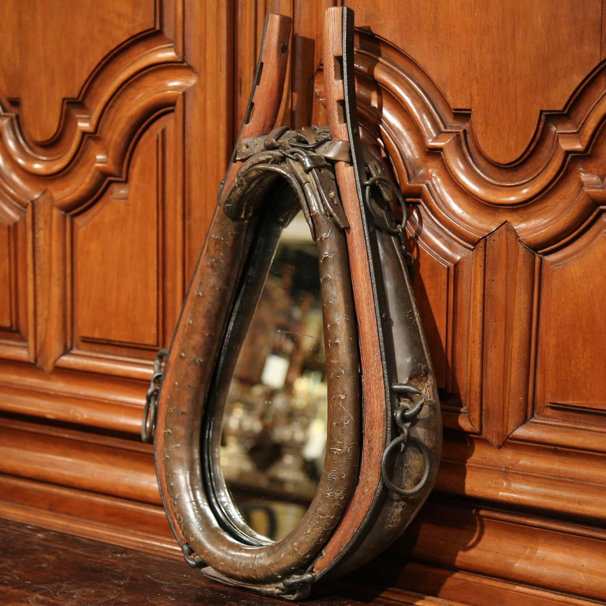 The wall hanging mirror is a unique find for the rustic home. The mirror is framed by a fine, antique horse collar from France, circa 1880. The collar is carved in wood and covered with leather and original hooks. This collar has been transformed