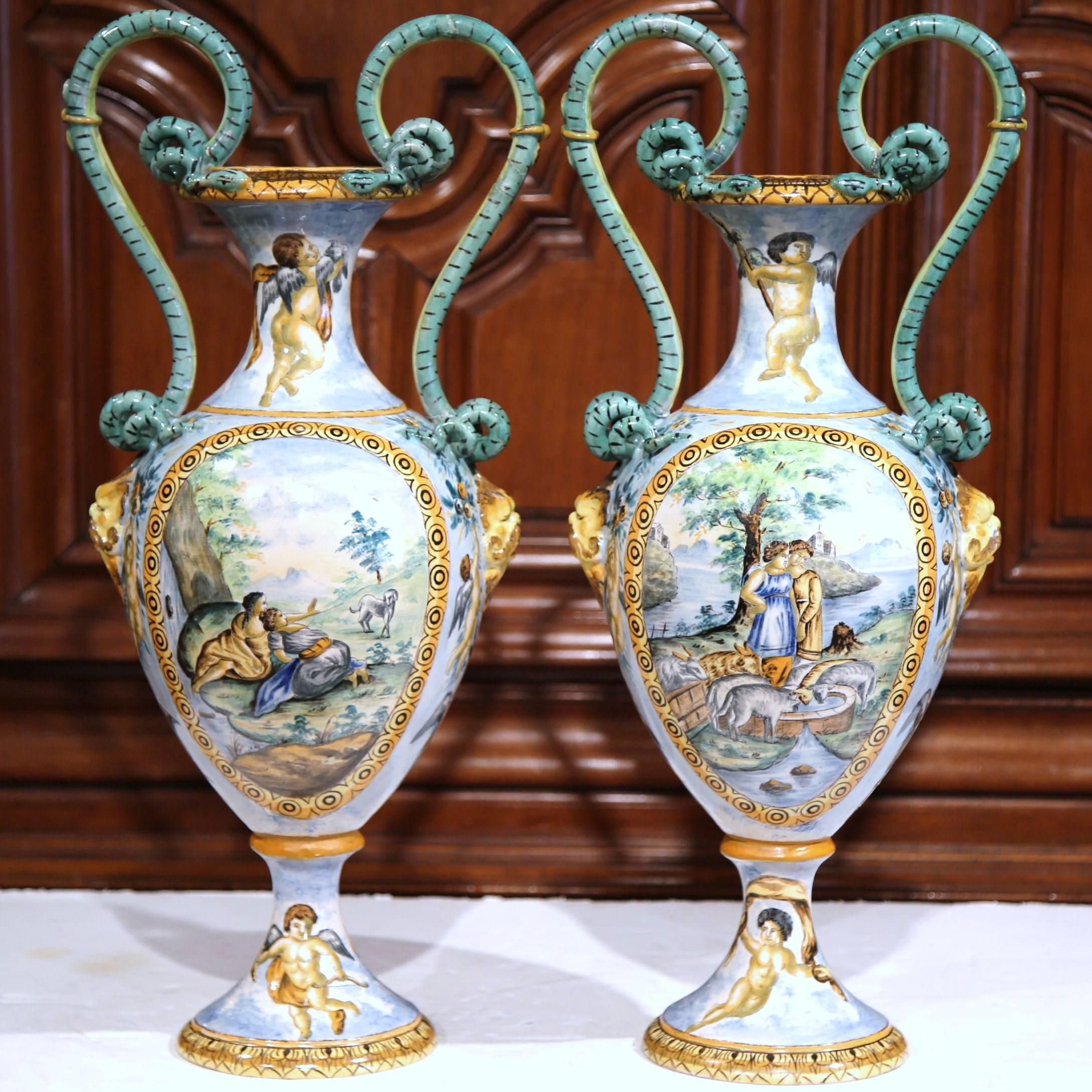 This delicate pair of antique hand-painted porcelain vases were sculpted in Italy, circa 1870. Each classical vase features colorful cherubs picking fruit from the trees, a Roman scene with chariot and horses, and a rustic, pastoral scene with