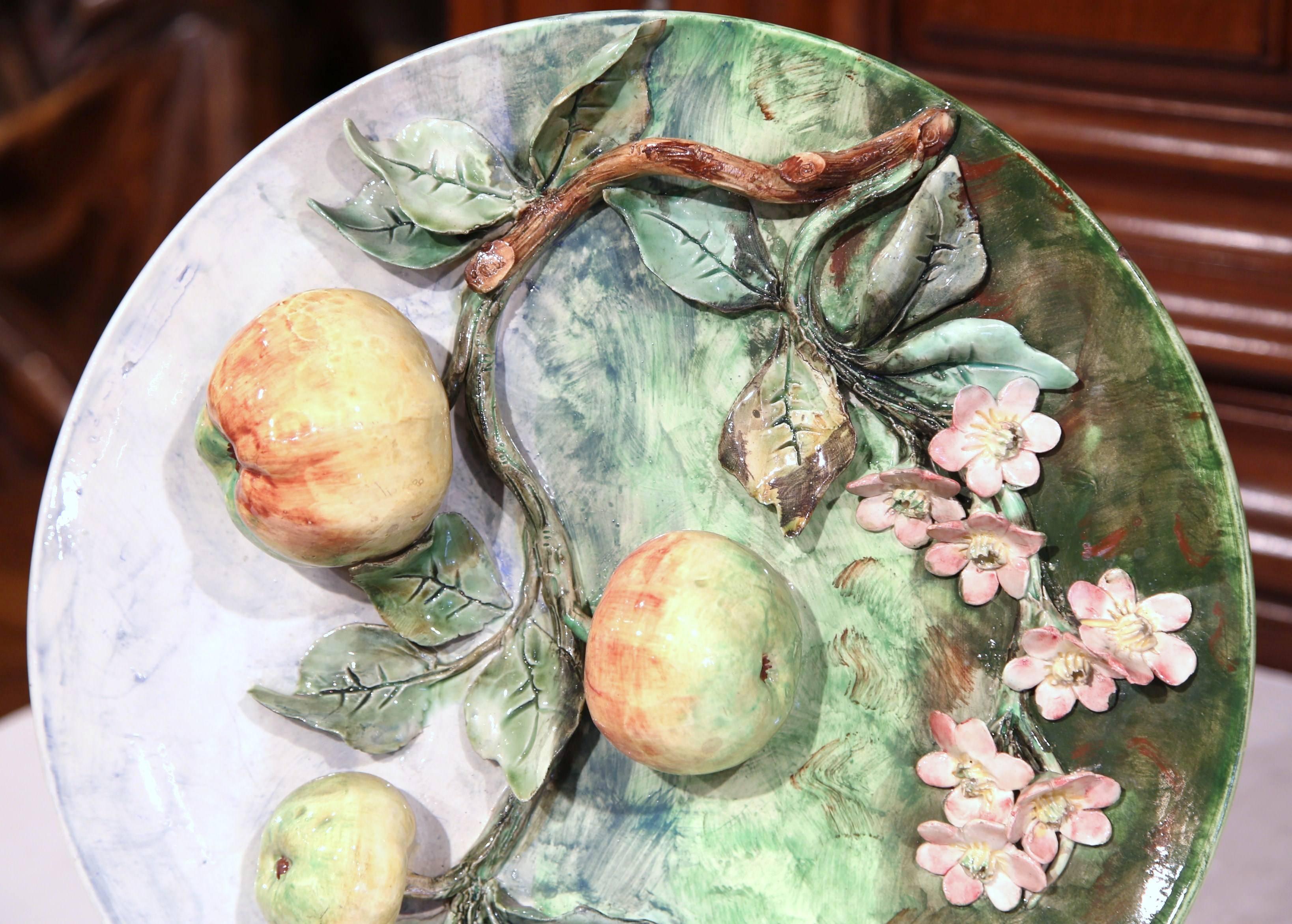 This colorful, antique Majolica plate was sculpted in France, circa 1880. The round, hand painted platter has pink flowers and three orange and yellow apples hanging from a tree branch covered with green leaves. The sculpted additions are in high