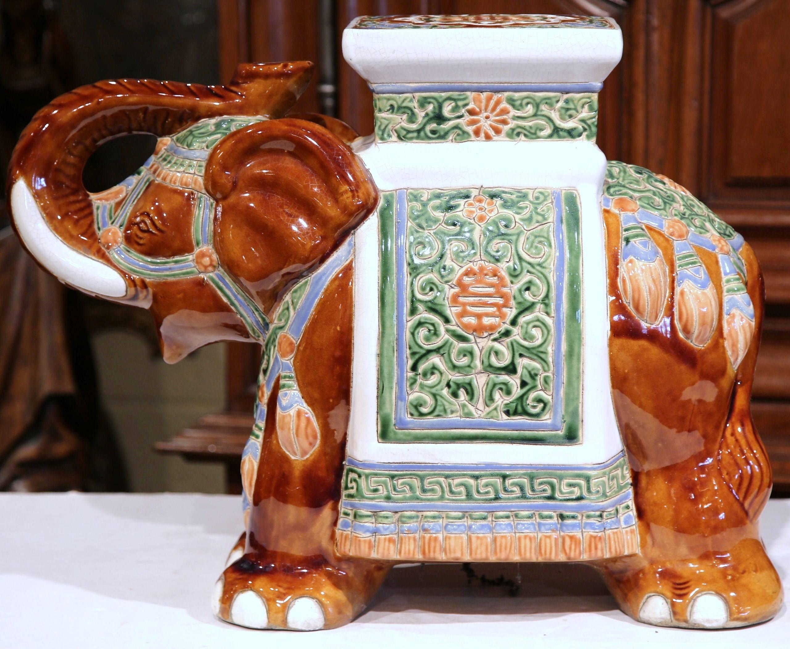 This elegant porcelain garden seat was sculpted in France, circa 1920. The piece is in the shape of an elephant raising his trunk, which is heavily decorated in oriental finery. The mammal has a square seat at the top, and is hand painted in a