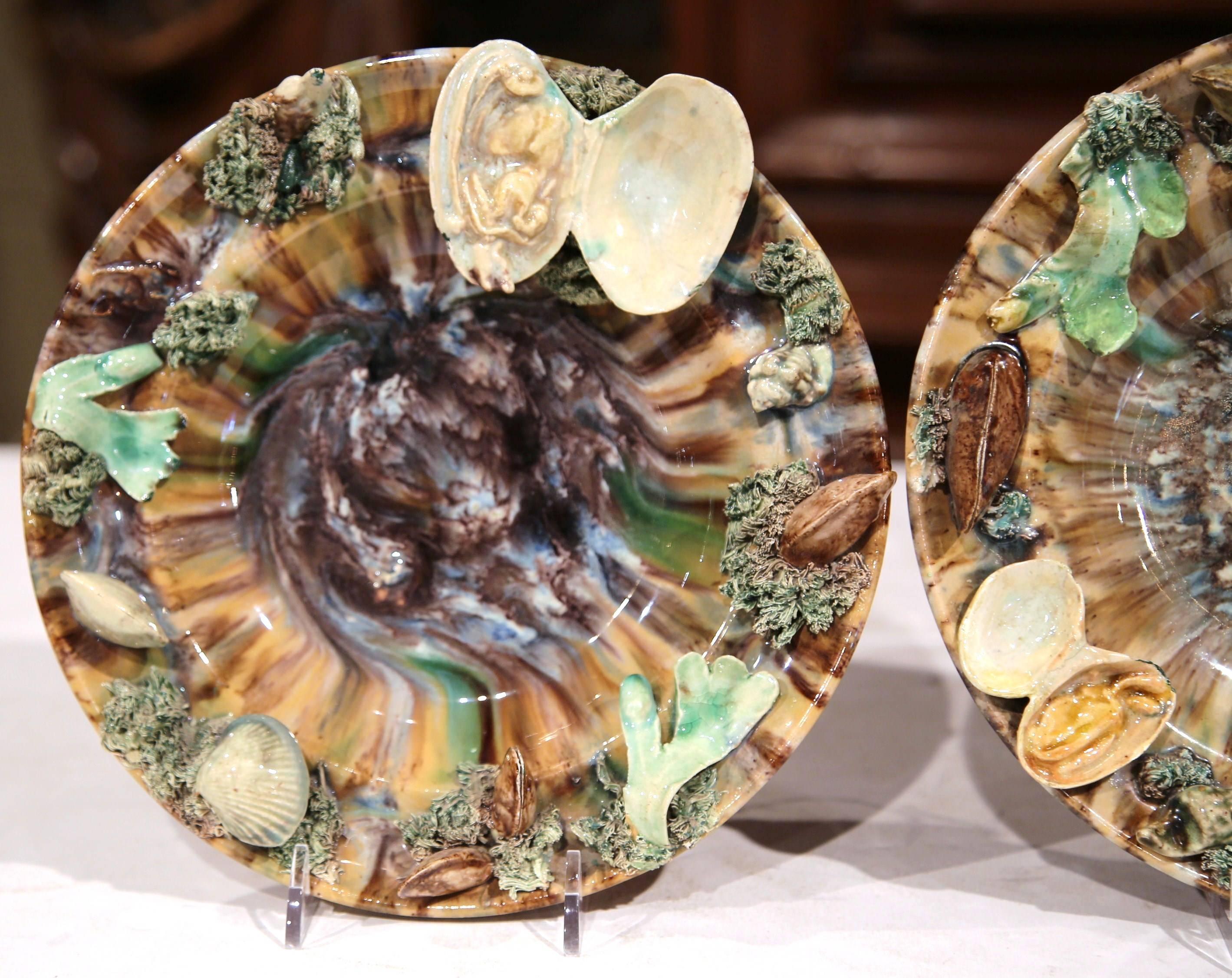 This colorful pair of Majolica wall hanging plates was sculpted in France, circa 1920. Perfect for a seaside beach home, these colorful ceramic plates are embellished with seashells and seaweed shaped in high relief. The plates decorated in Palissy