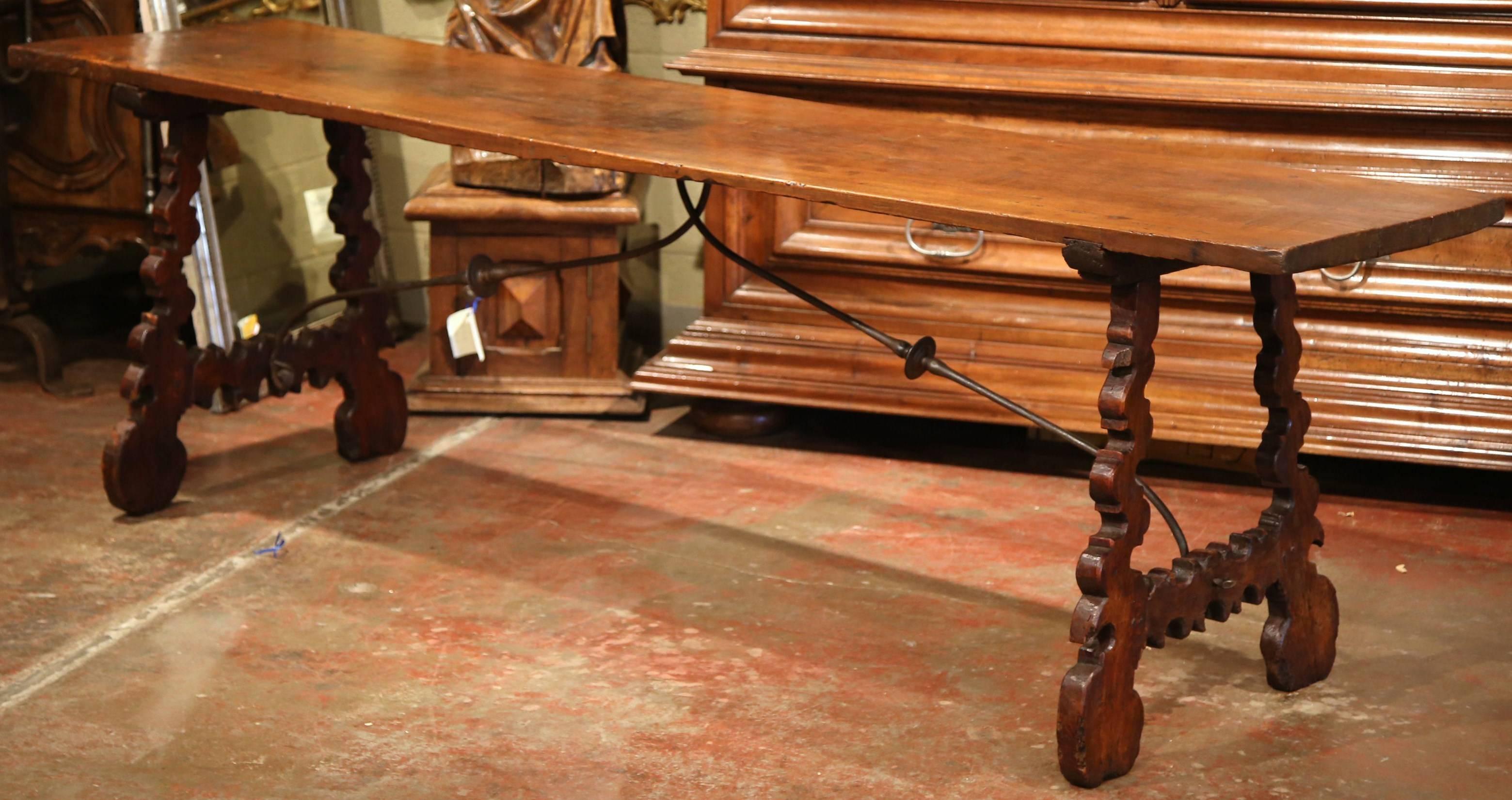 This long and narrow antique fruitwood table was crafted in Spain, circa 1780. The elegant table features two carved, A-shape legs built of pine, which are connected in the centre with a forged black wrought iron stretcher for stability and