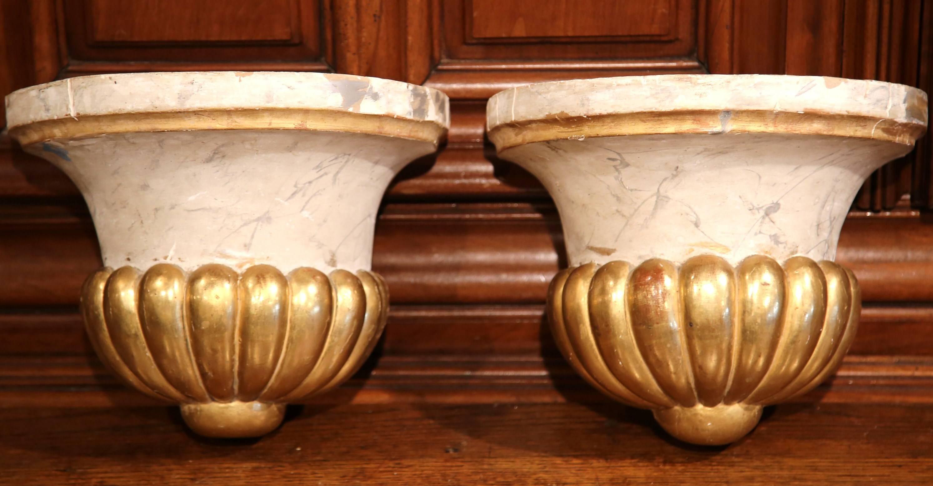 This beautiful pair of antique wall hanging brackets were crafted in France circa 1830. Each of the hand carved corbels features a cream faux marble finish with gold leaf embellishment on the bottom. The pots have a large mouth and a scalloped